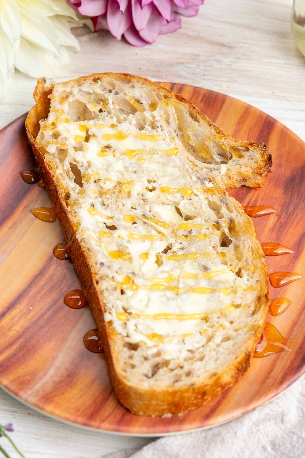 Slice of lavender vanilla sourdough bread on a plate with butter and a drizzle of honey.