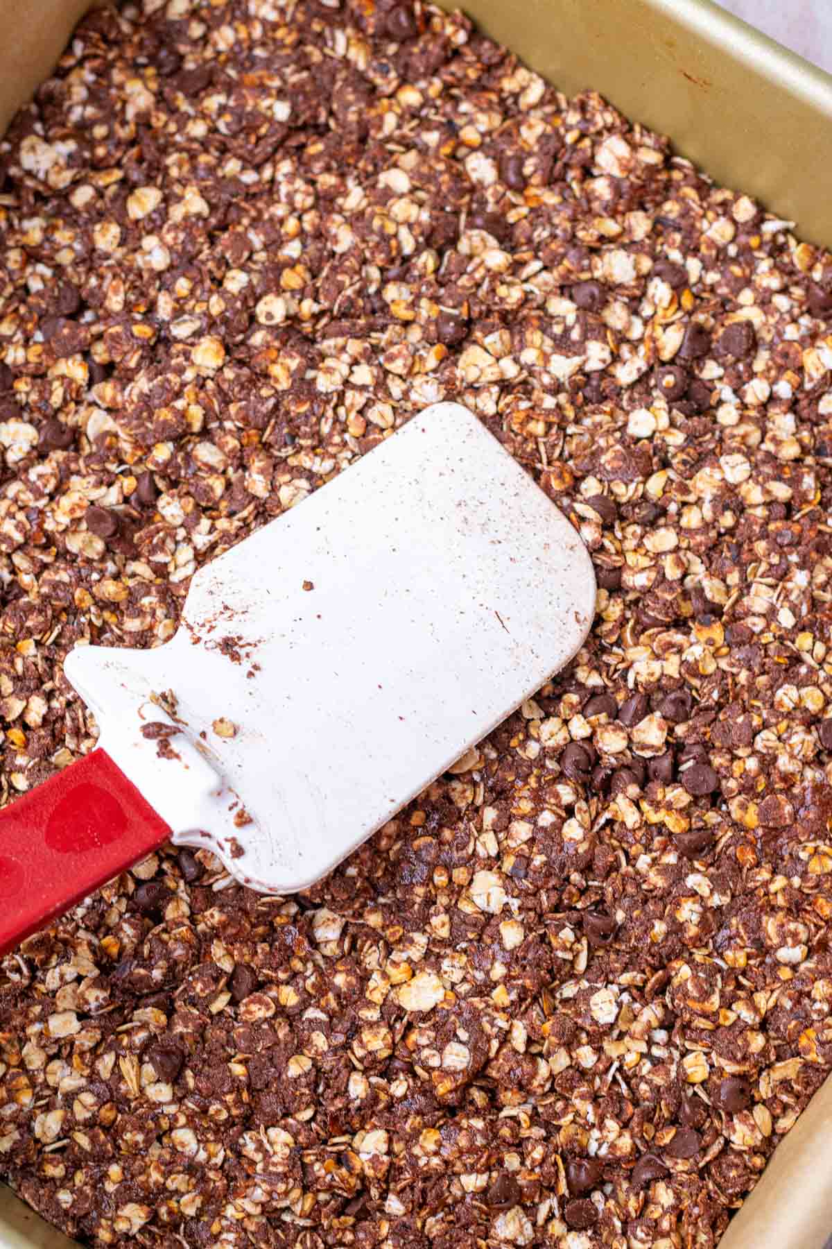 Spatula pressing down on sourdough granola bars in pan.