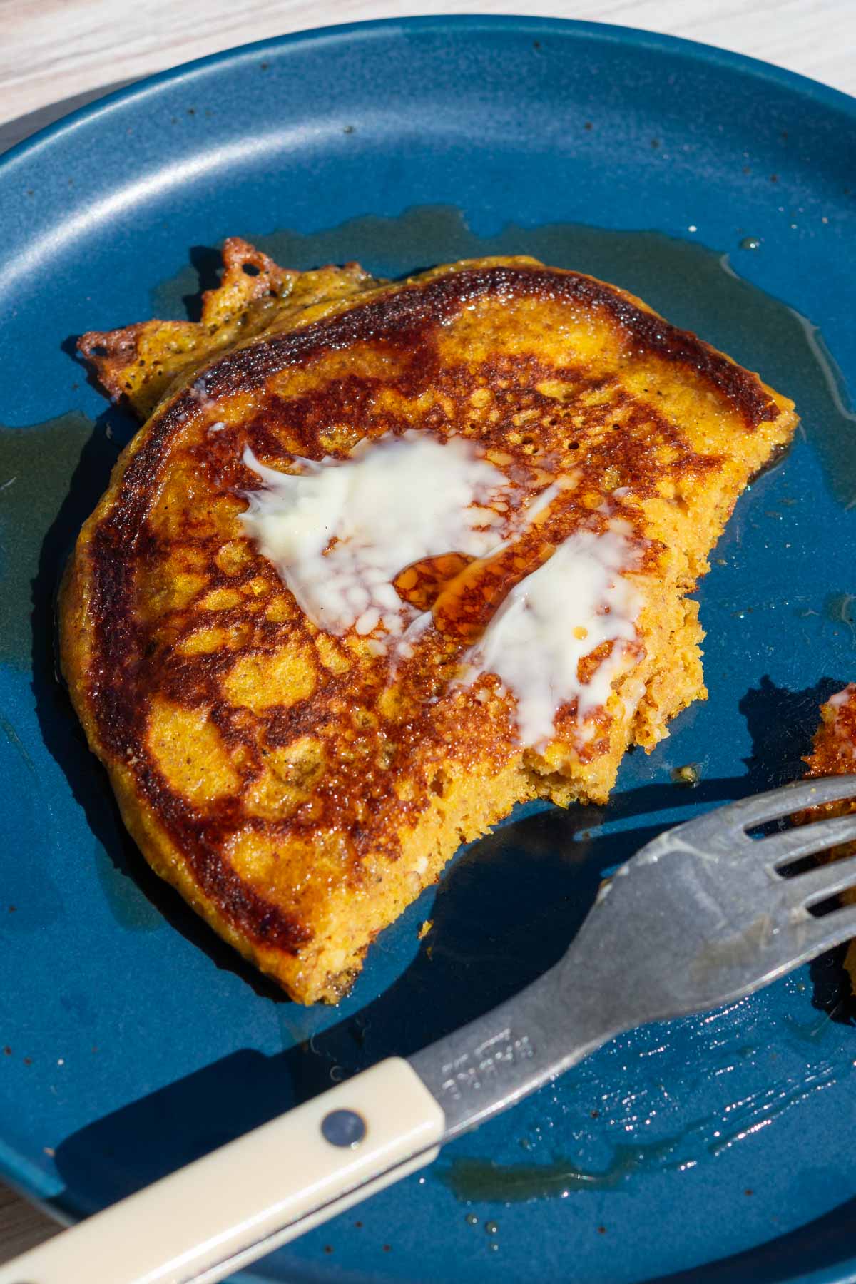 Fork taking bites out of a sourdough pumpkin pancake on a plate with maple syrup and butter.
