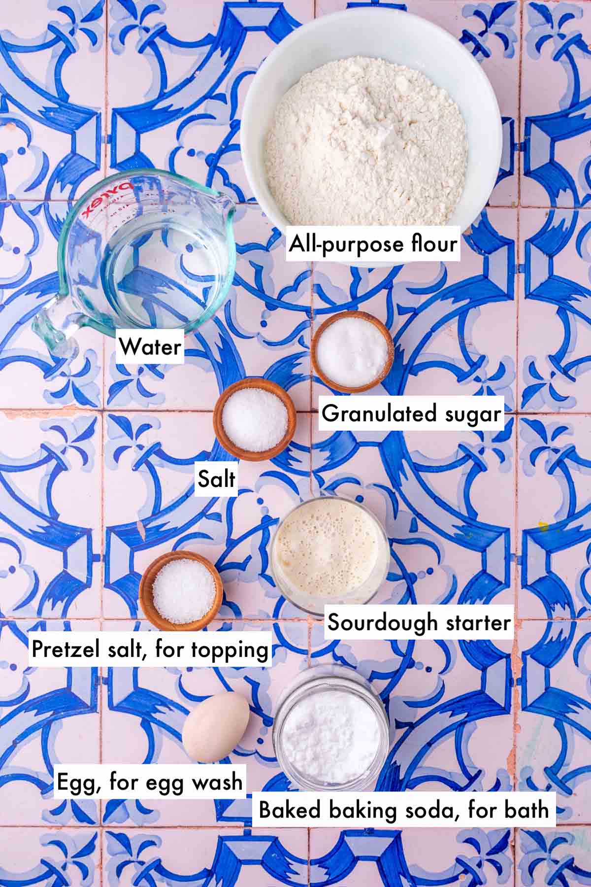 Labeled bowls of ingredients for sourdough pretzel rods including all-purpose flour, water, pretzel salt, salt, baked baking soda, egg wash, granulated sugar, and sourdough starter.