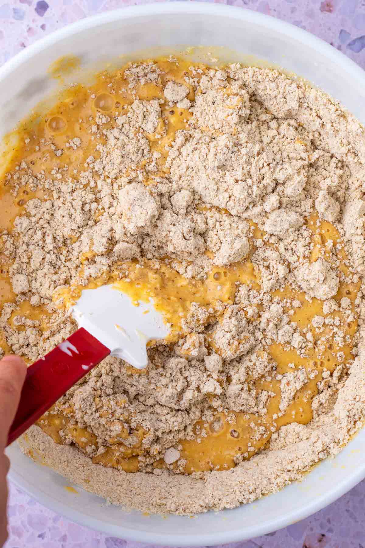 Mixing the wet and dry ingredients for sourdough pumpkin pancakes together in a large bowl with a spatula.