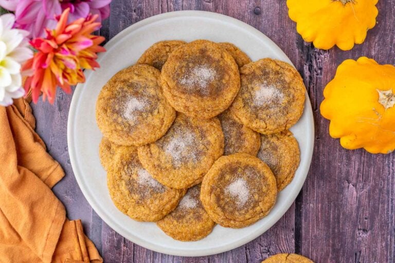 Plate of sourdough pumpkin maple cookies with an orange towel, pumpkins, and flowers.