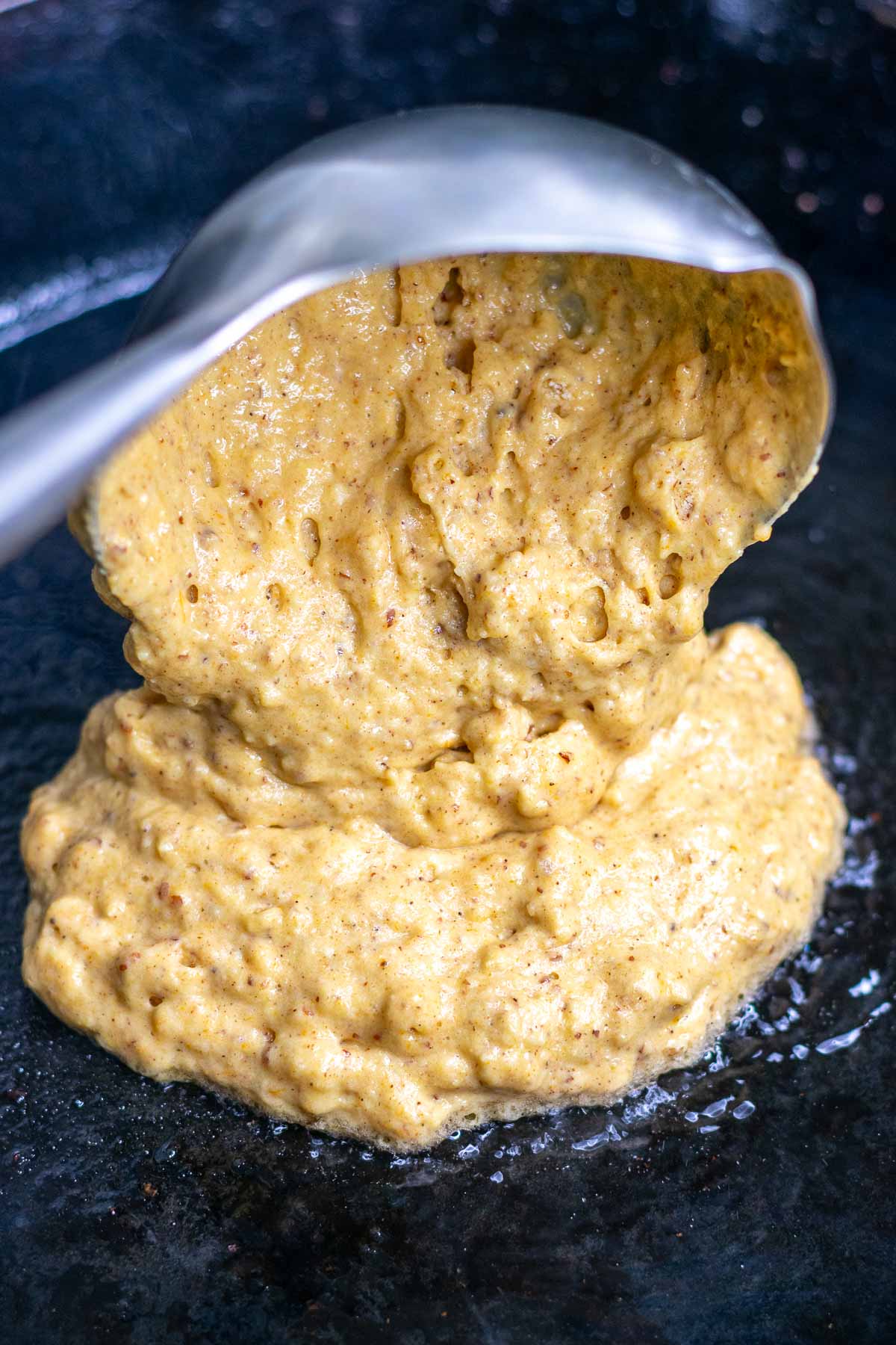 Pouring sourdough pumpkin pancake batter in cast-iron skillet with a ladle.