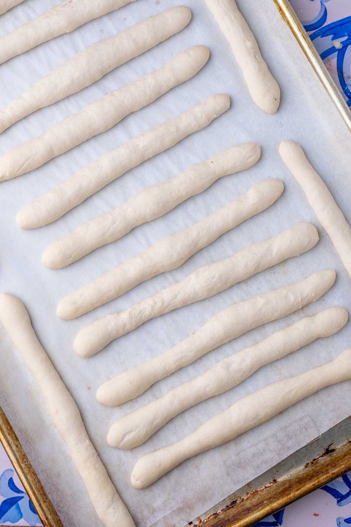 Proofed sourdough pretzel rods on a baking sheet.