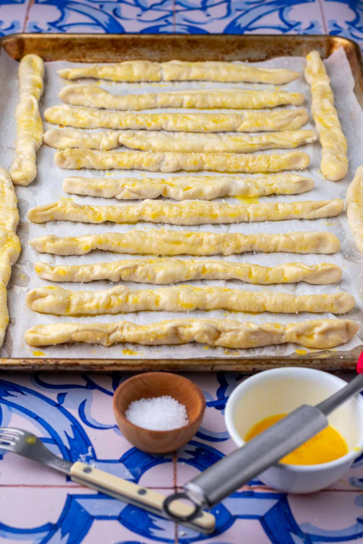 Egg wash on sourdough pretzel rods on a baking sheet.