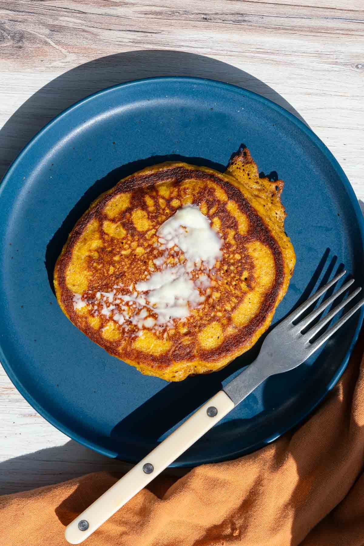 A sourdough pumpkin pecan pancake with butter on a plate with a fork.