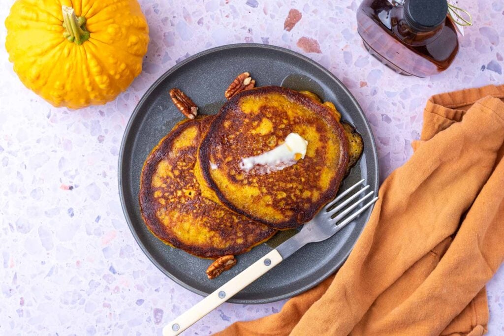 Sourdough pumpkin pancakes on a plate with butter, pecans, and maple syrup.