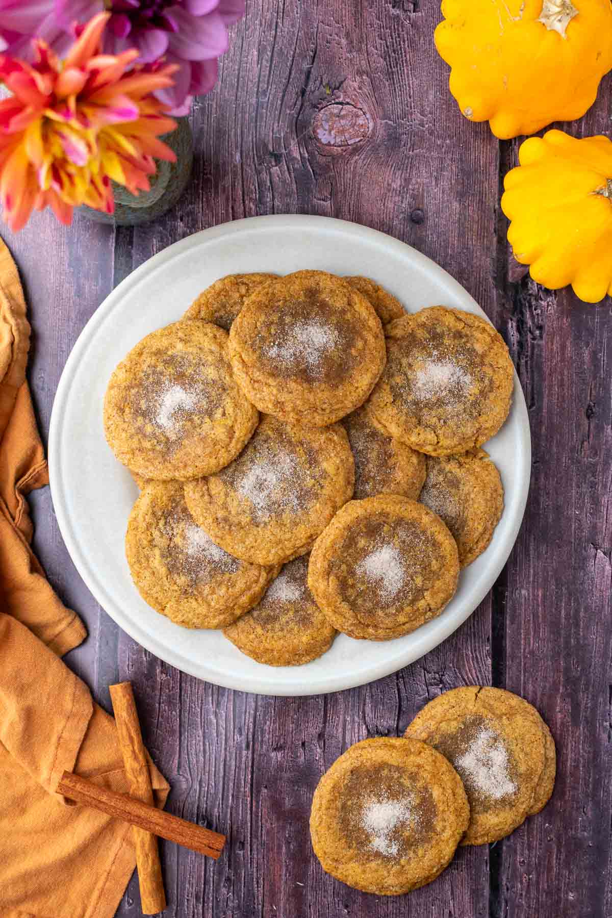 Sourdough discard pumpkin maple cookies on a plate with an orange towel, flowers, and pumpkins.