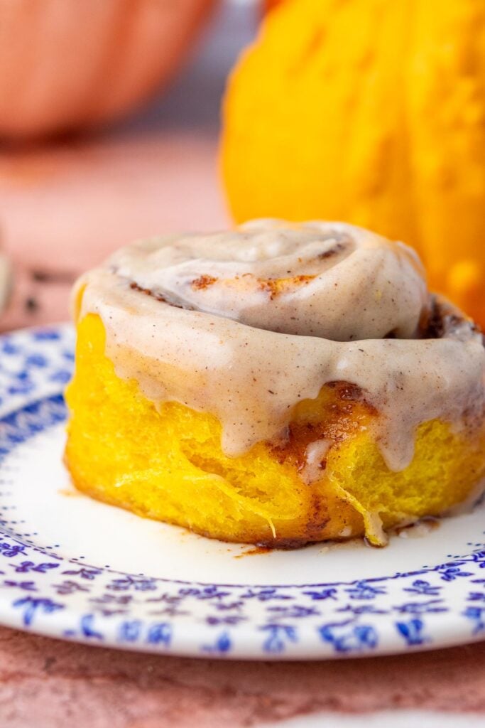 Close up of a Sourdough pumpkin cinnamon roll on a plate with dripping chai cream cheese frosting.