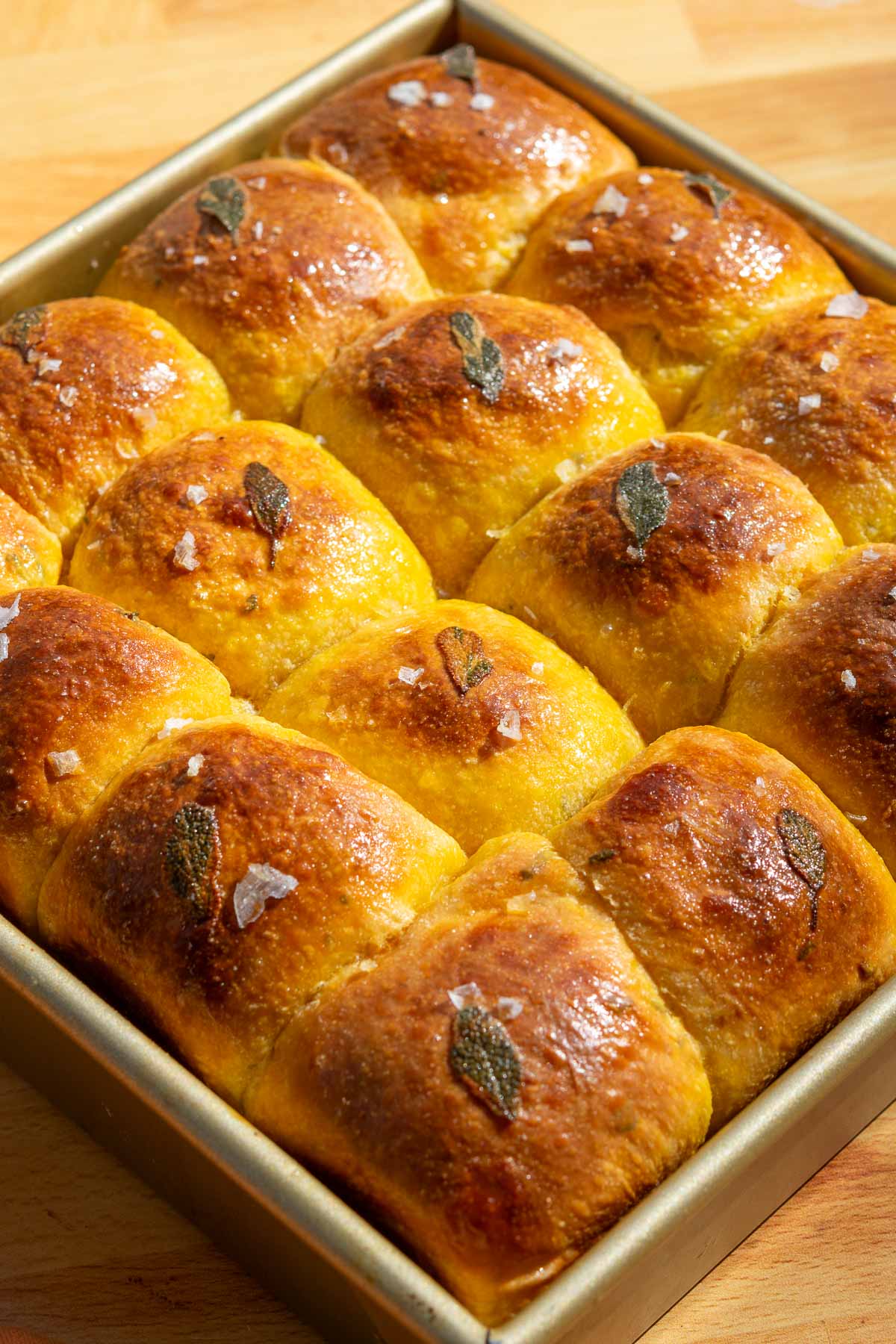 Baked sourdough sweet potato dinner rolls with sage in pan.