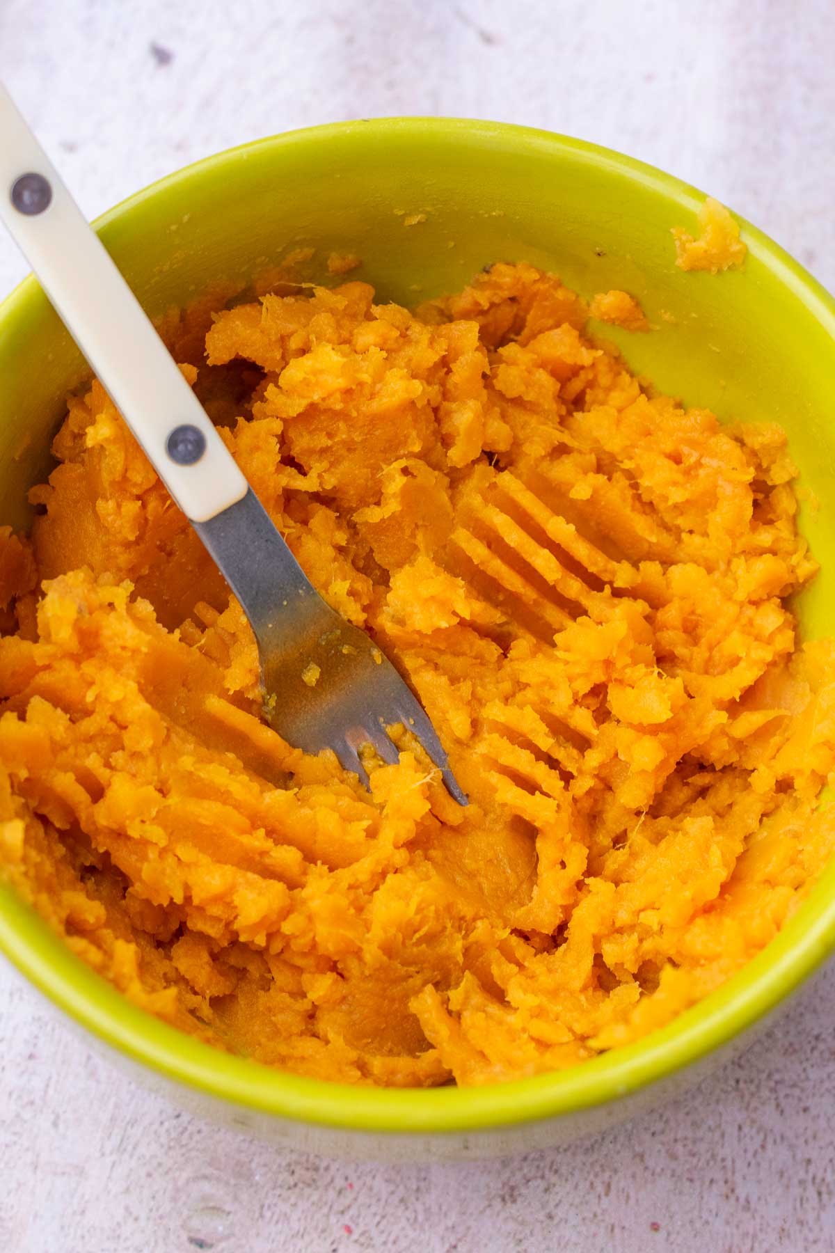 Bowl of mashed sweet potatoes with a fork.