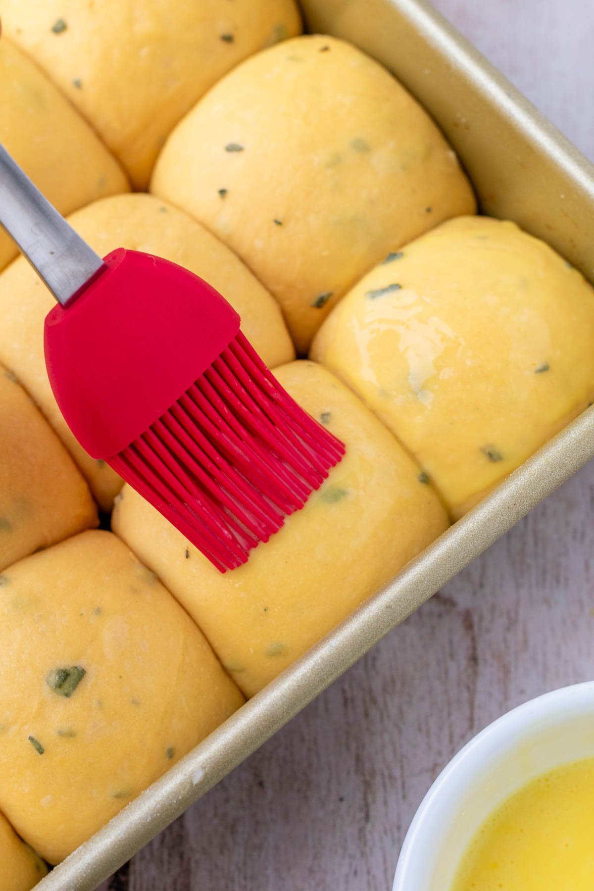 Brushing egg wash on sourdough sweet potato dinner rolls.