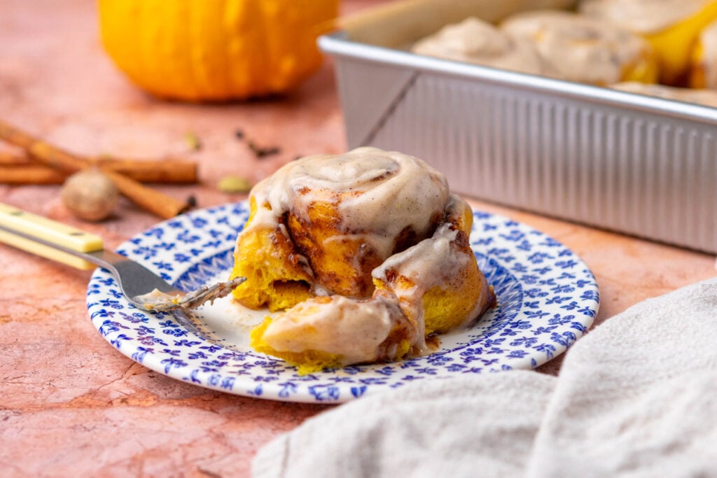 Sourdough pumpkin cinnamon roll with chai cream cheese frosting on a plate with a fork and bite taken out.