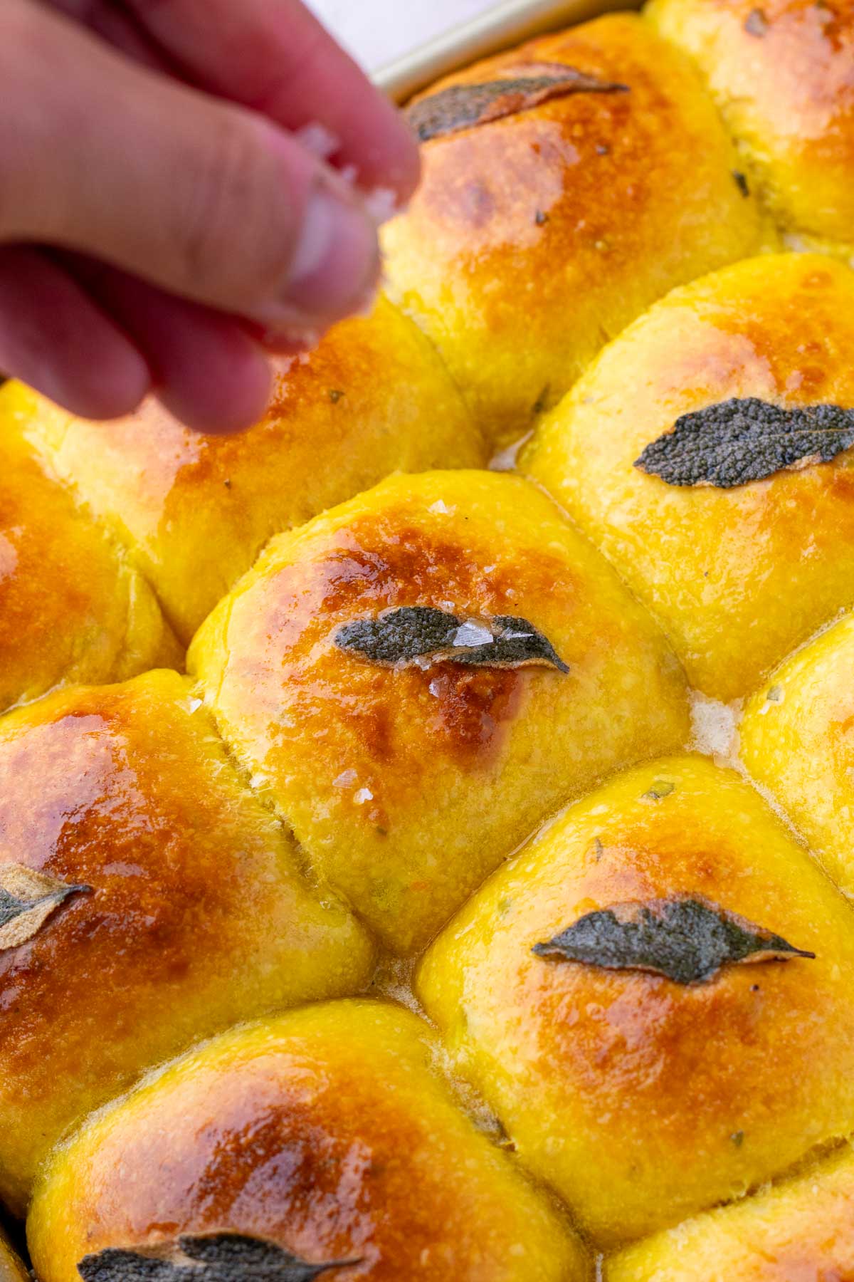 Sprinkling flaky salt on buttered sourdough sweet potato dinner rolls after bakig.