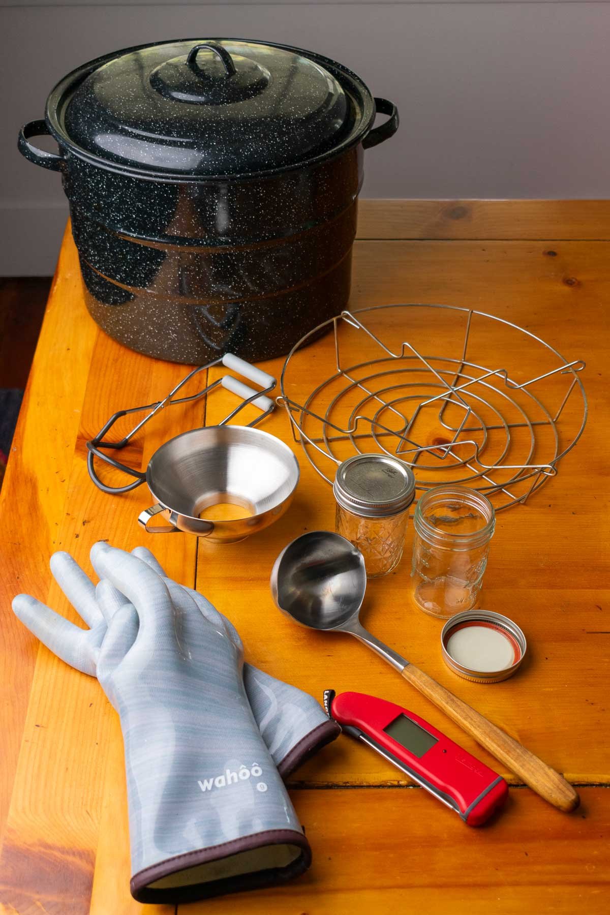 Tools needed for canning jam, including a large pot, canning rack, jar lifter, funnel, gloves, ladle, jars, and thermometer.