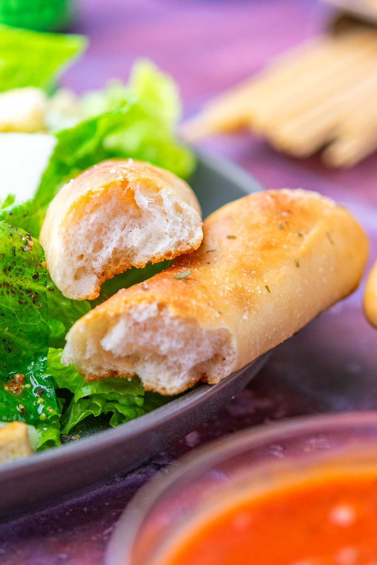 Sourdough breadstick torn in half on a plate with caesar salad.