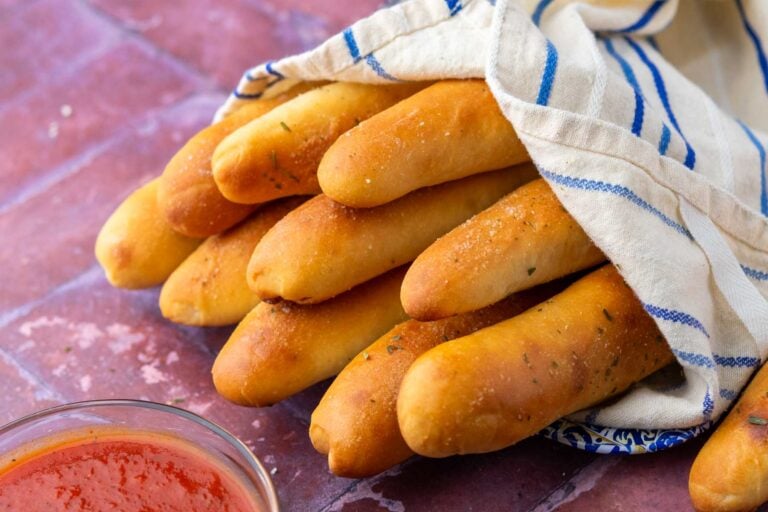 Sourdough breadsticks wrapped in towel with marinara sauce.
