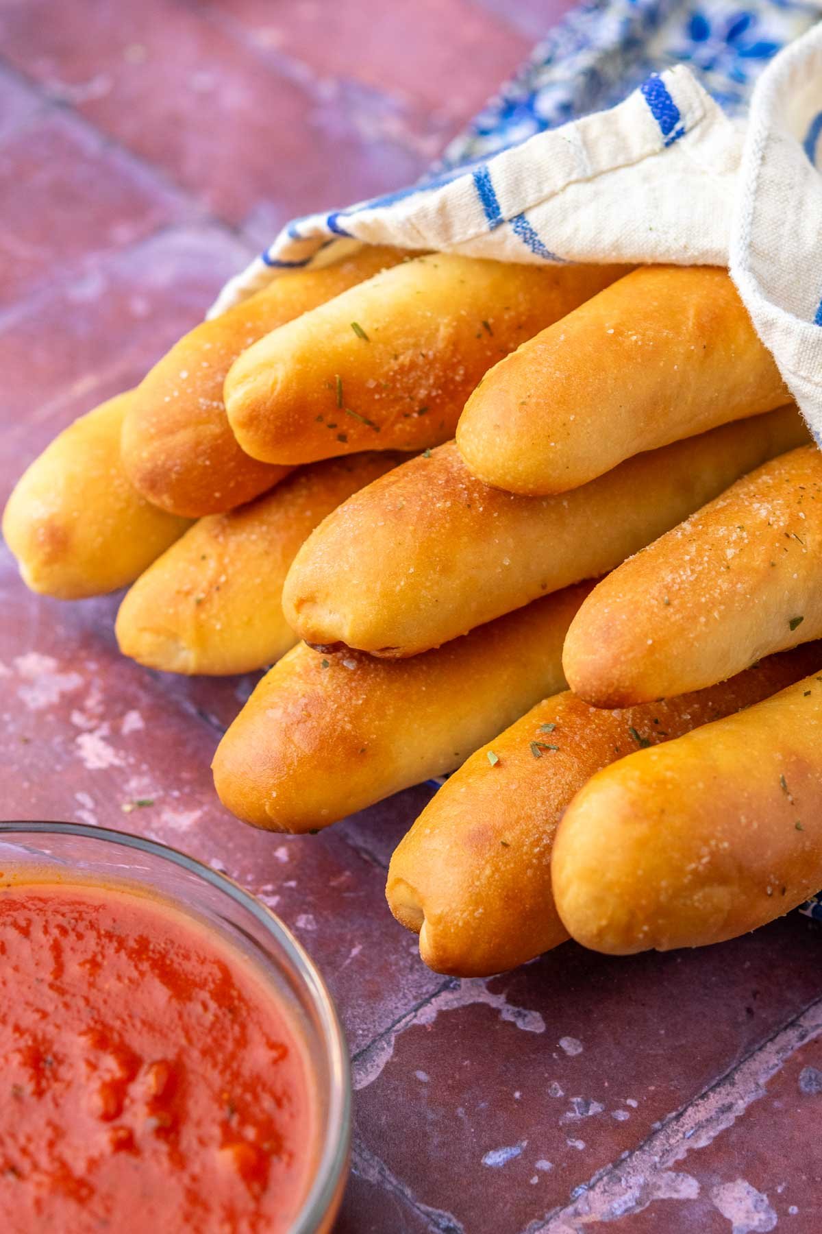 Sourdough breadsticks wrapped in a towel with a bowl marinara sauce.