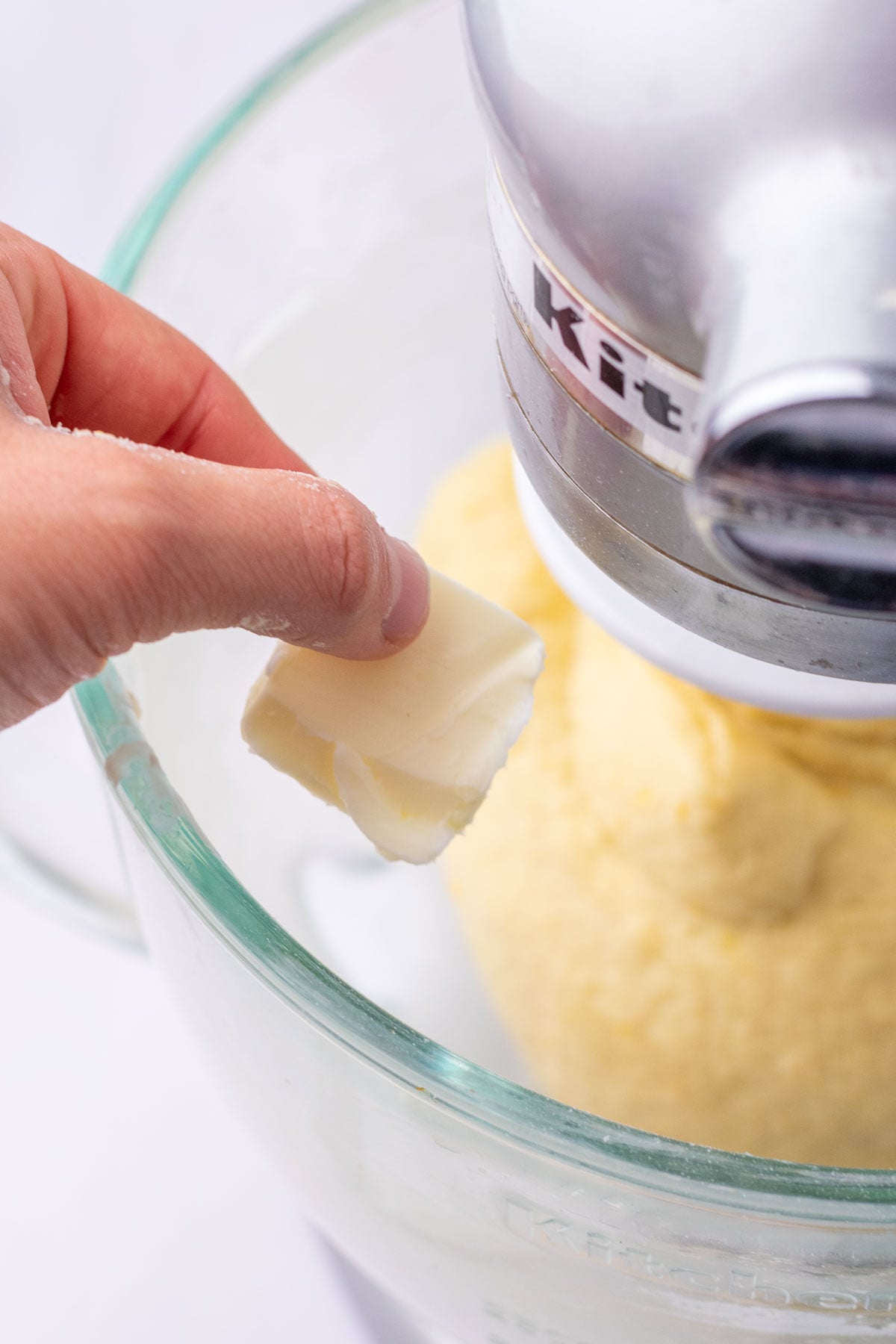 Hand adding a tablespoon of butter to mixing dough.
