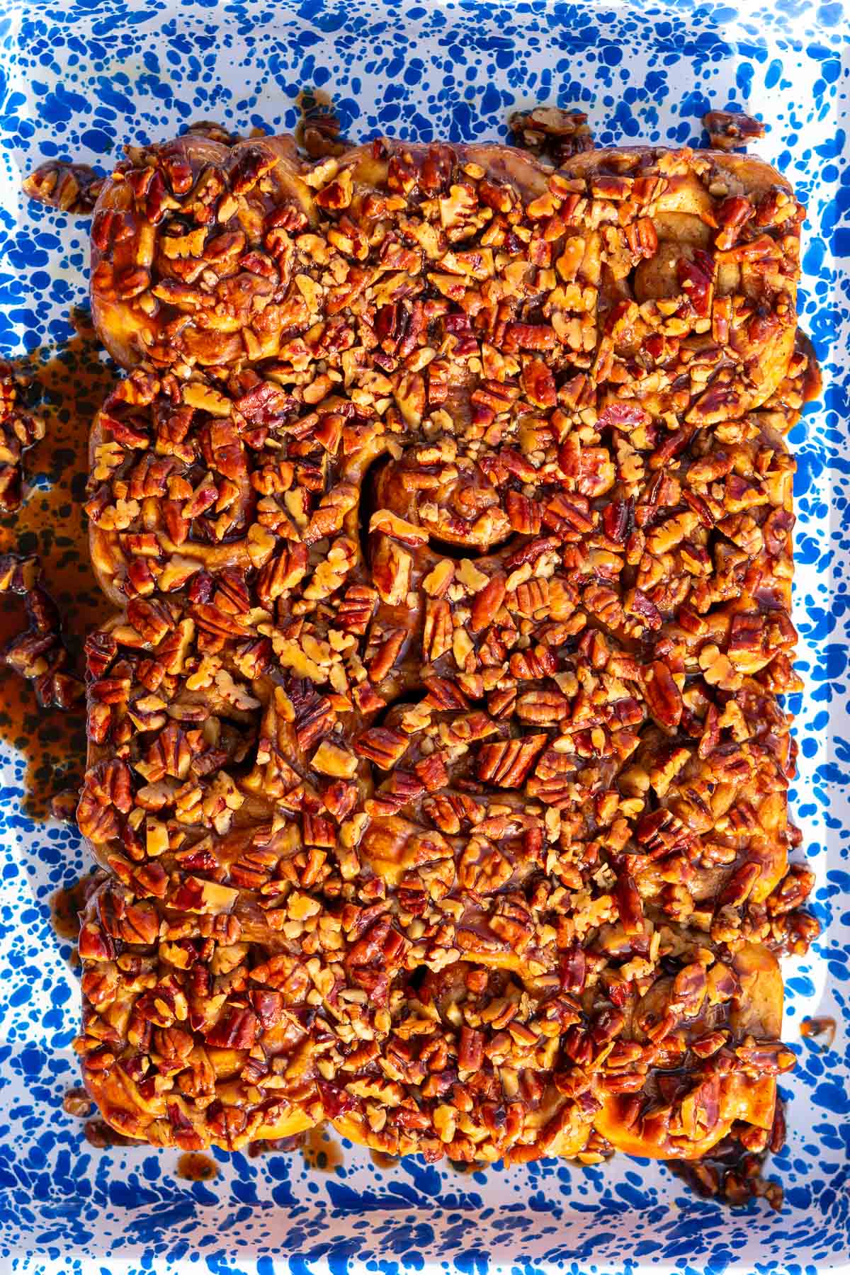 Baked sourdough maple pecan sticky buns flipped over on an enamel splatterware platter.