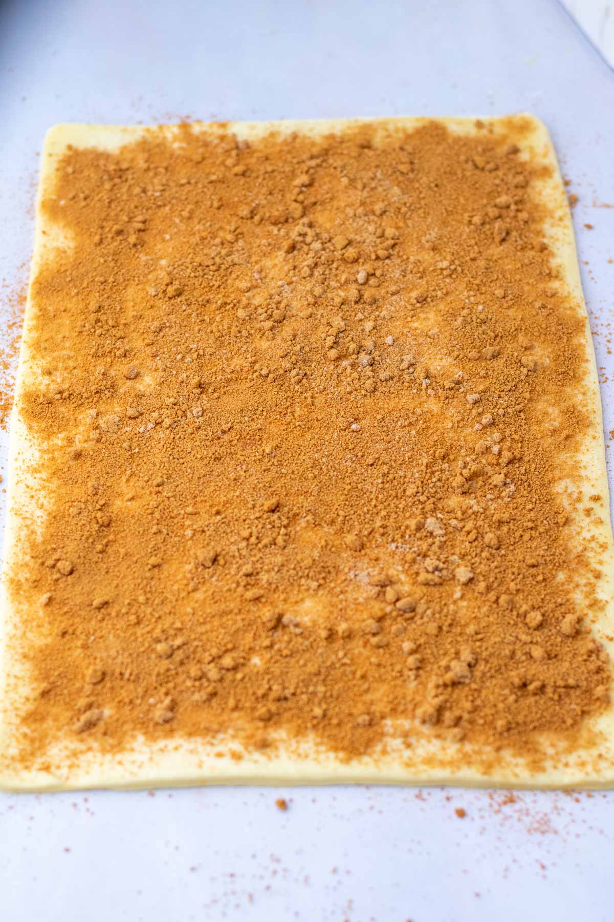 Cinnamon sugar filling sprinkled on sticky bun slab of dough before rolling up.