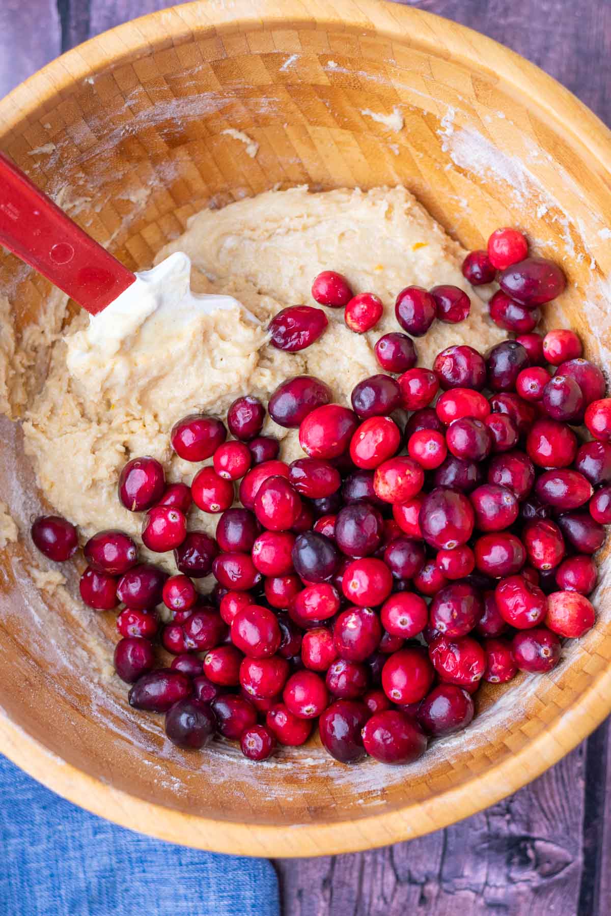 Folding fresh cranberries with a spatula into sourdough cranberry muffin batter in a large mixing bowl.