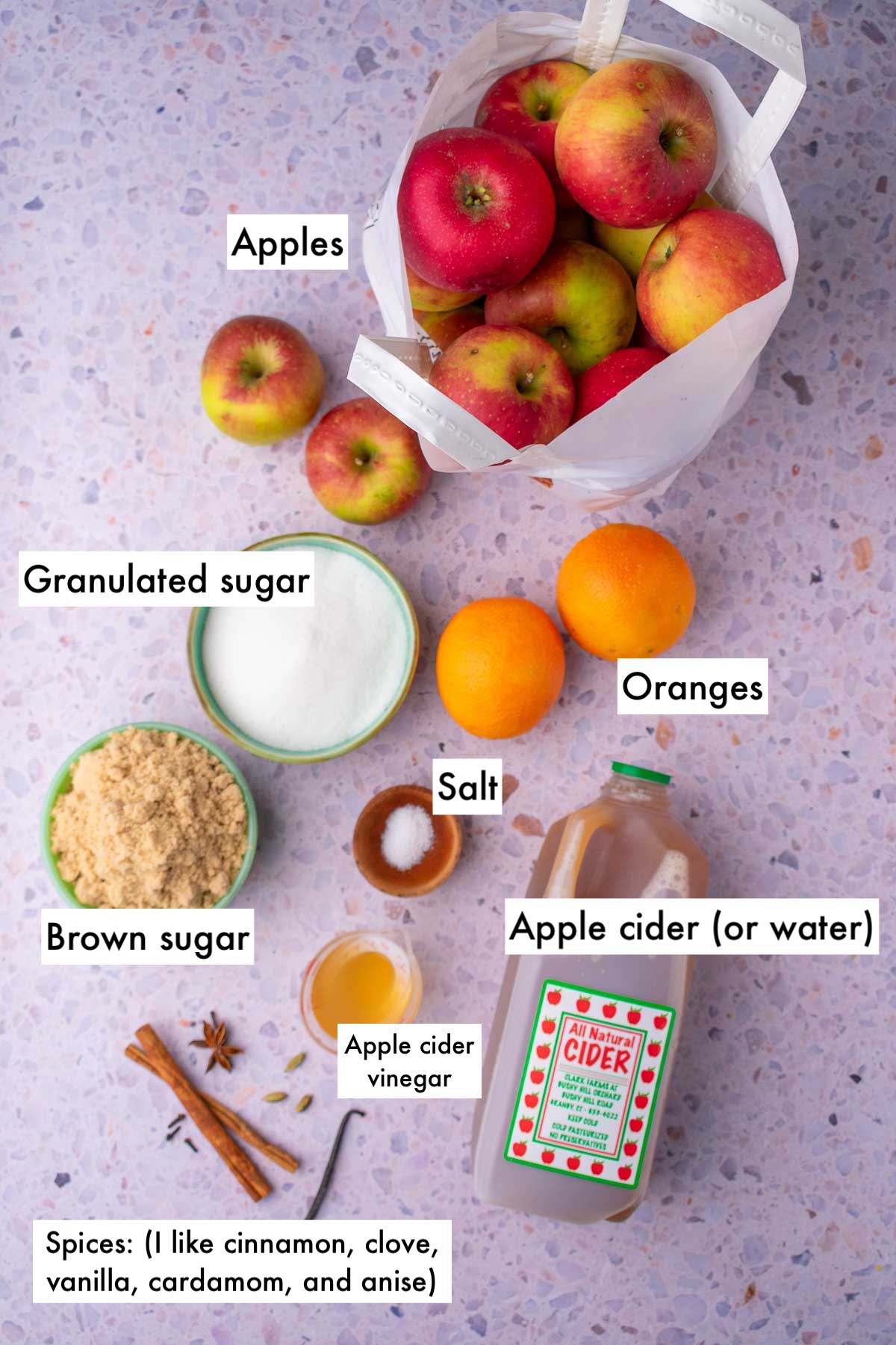 Labeled ingredients needed for apple butter including apples, oranges, sugar, brown sugar, apple cider, apple cider vinegar, salt, and spices.
