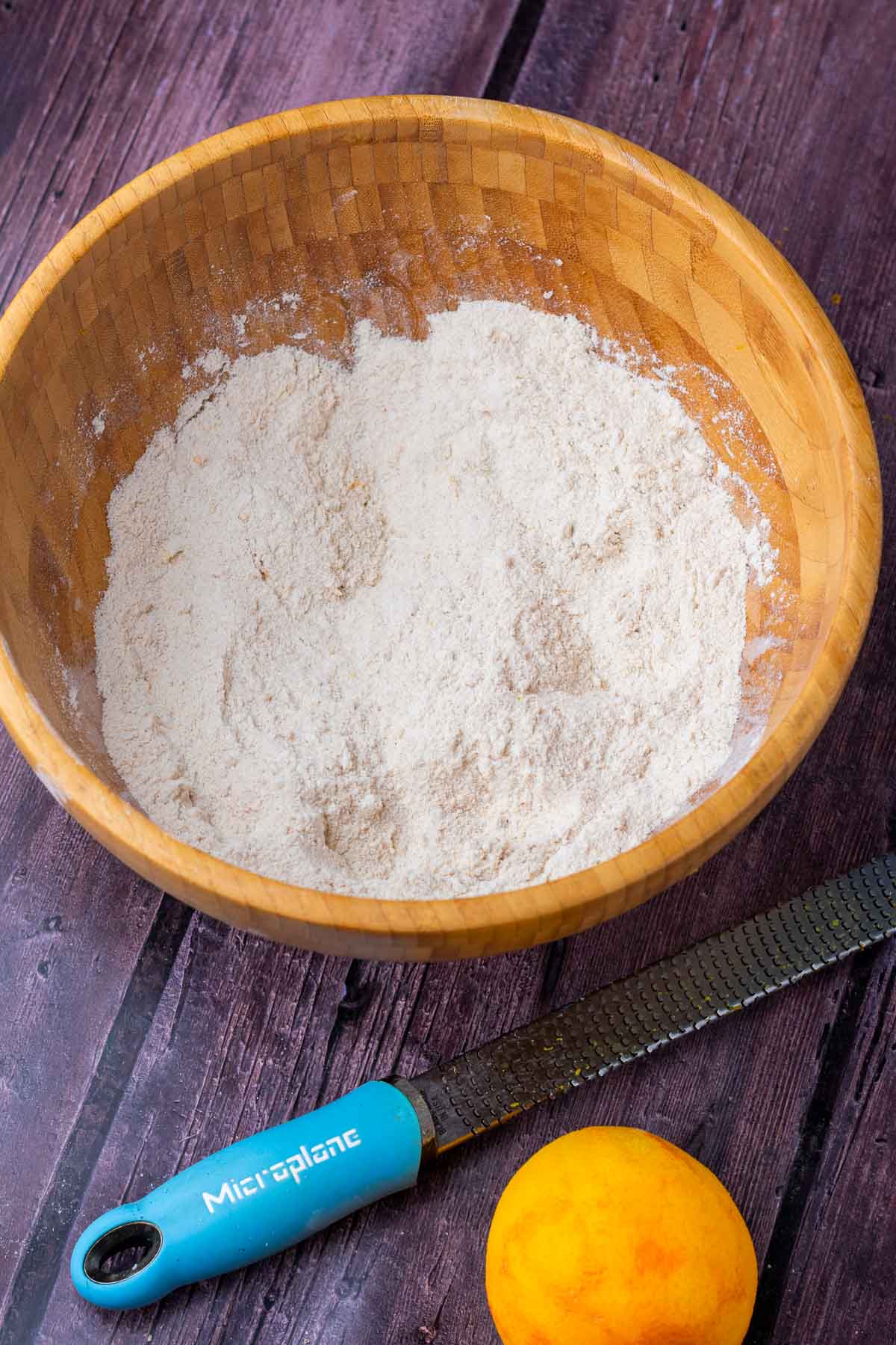 Large mixing bowl with dry ingredients mixed for sourdough cranberry muffins and an orange zested.