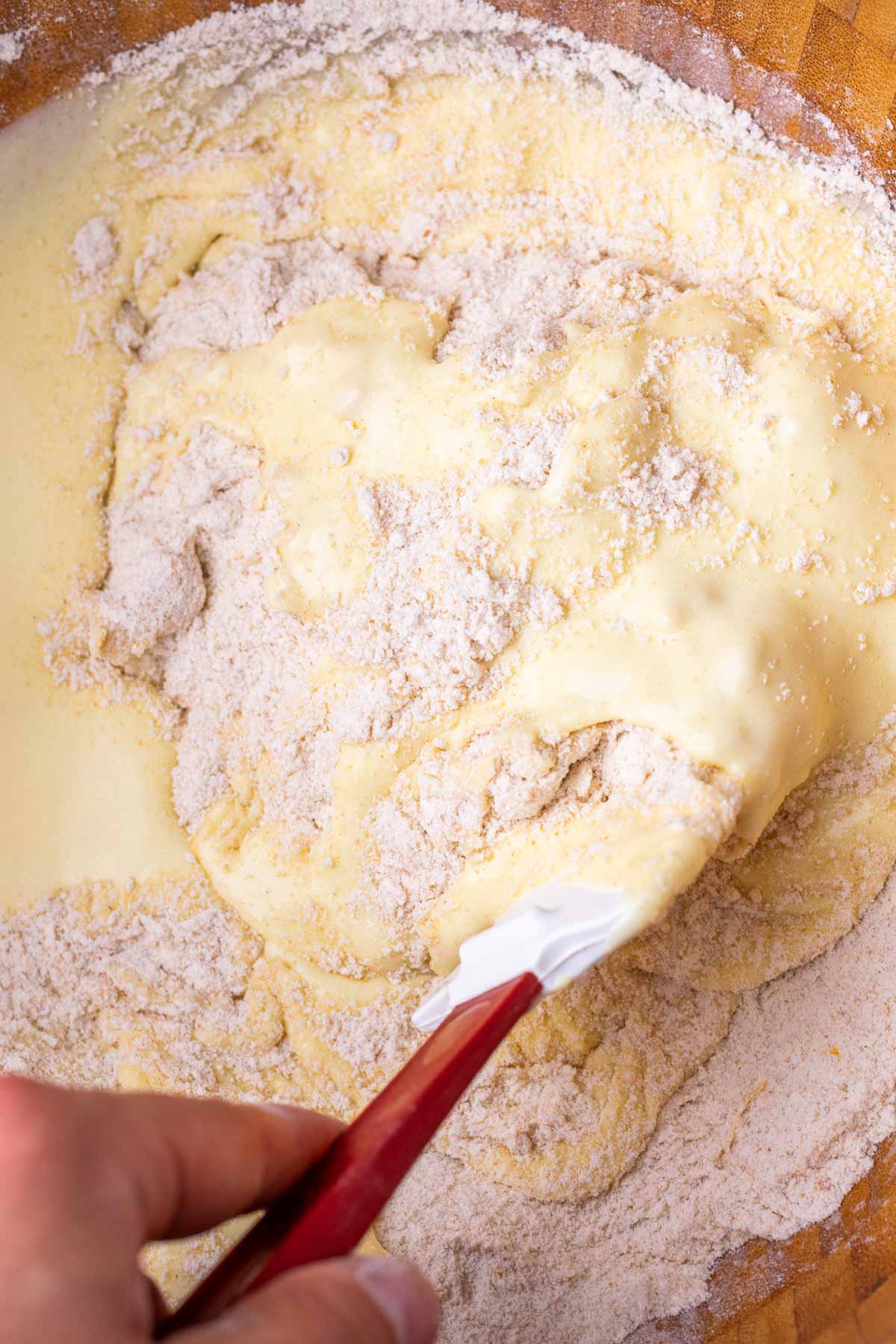 Mixing sourdough cranberry muffin batter with a spatula in a large mixing bowl.