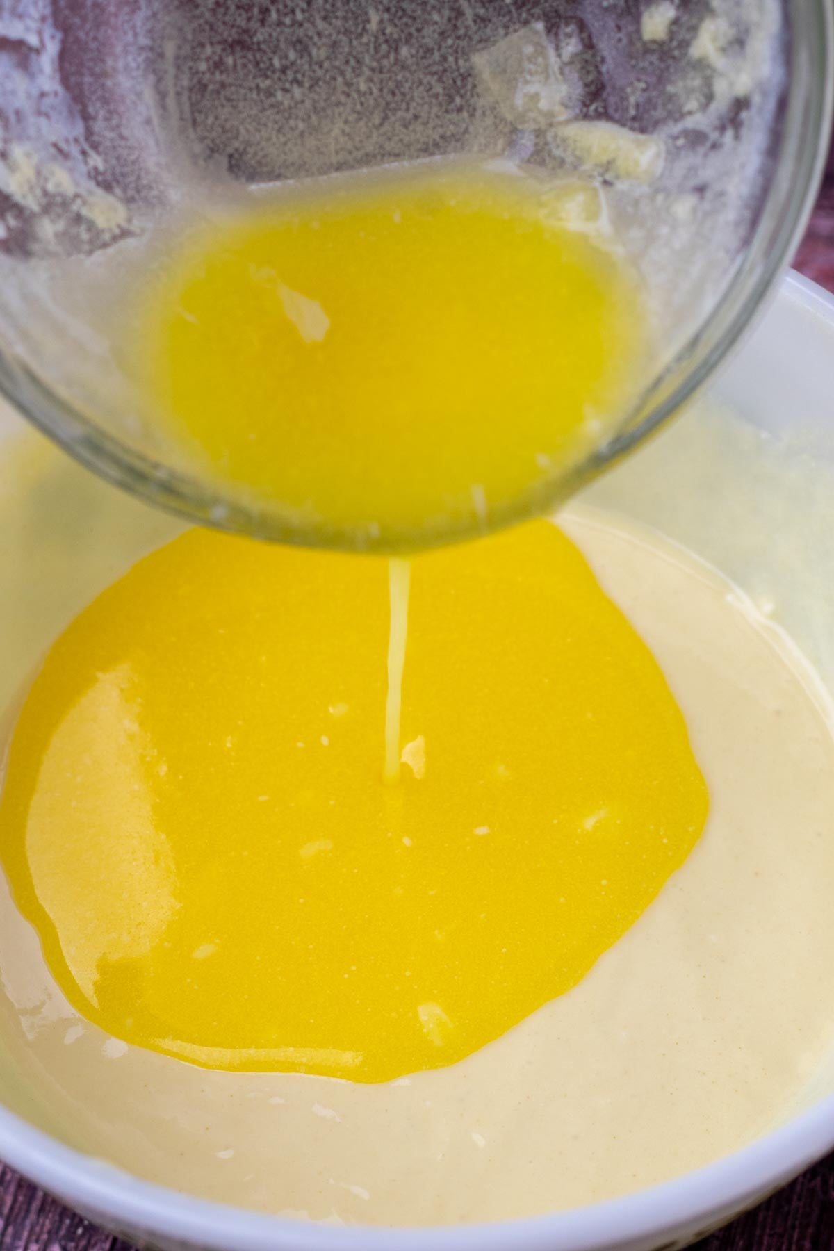 Pouring melted butter into bowl of wet ingredients for sourdough cranberry muffins.
