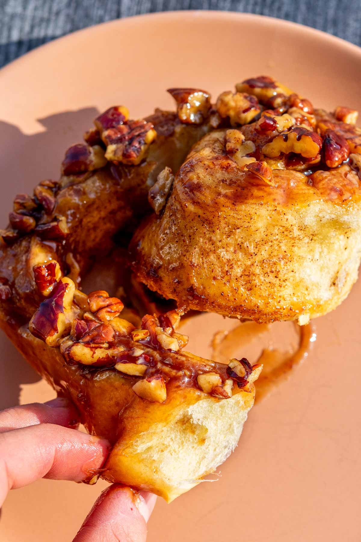 Hand pulling apart a Sourdough maple pecan sticky bun on a plate.