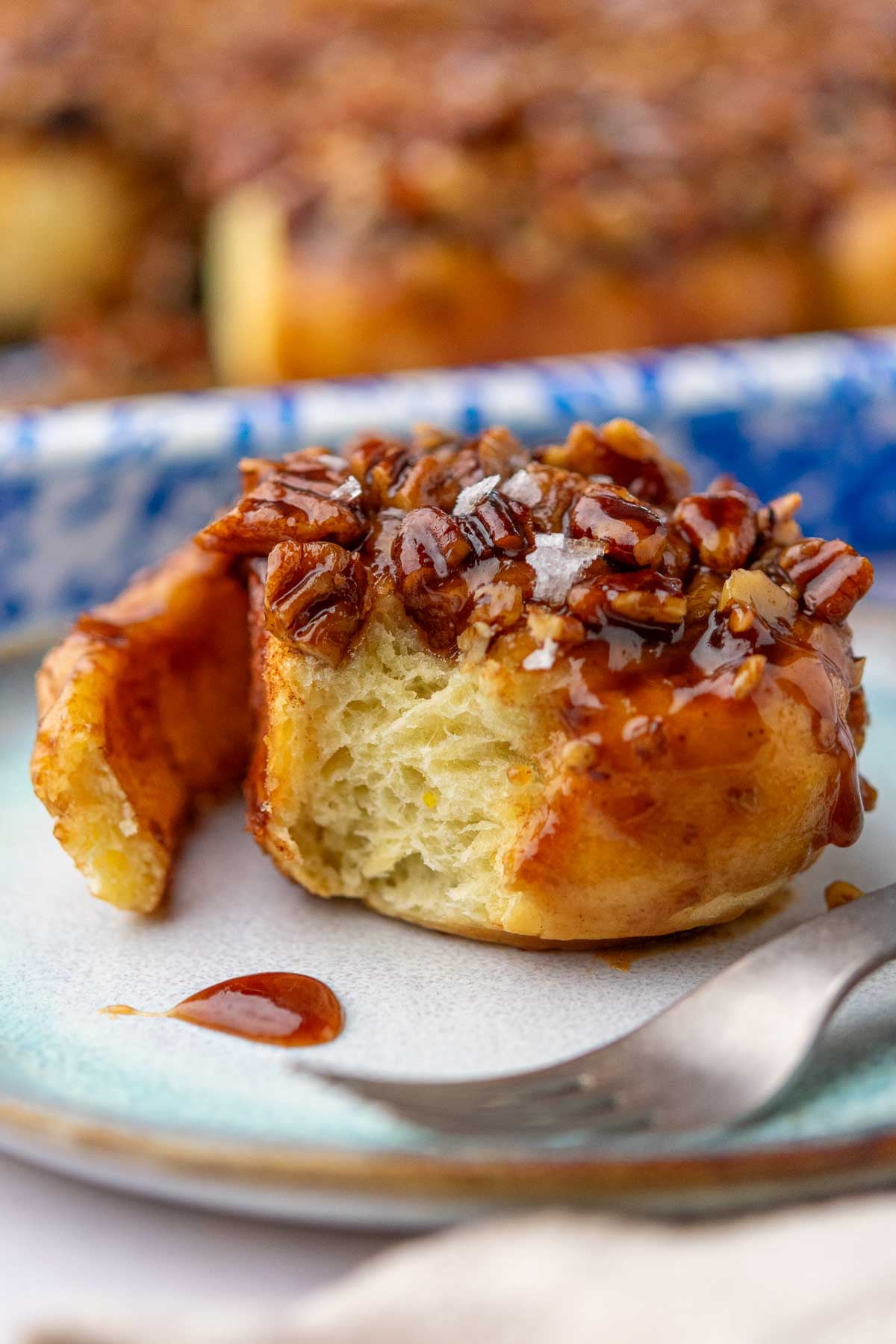Sourdough maple pecan sticky bun on a plate with fork and a bite taken out of it.
