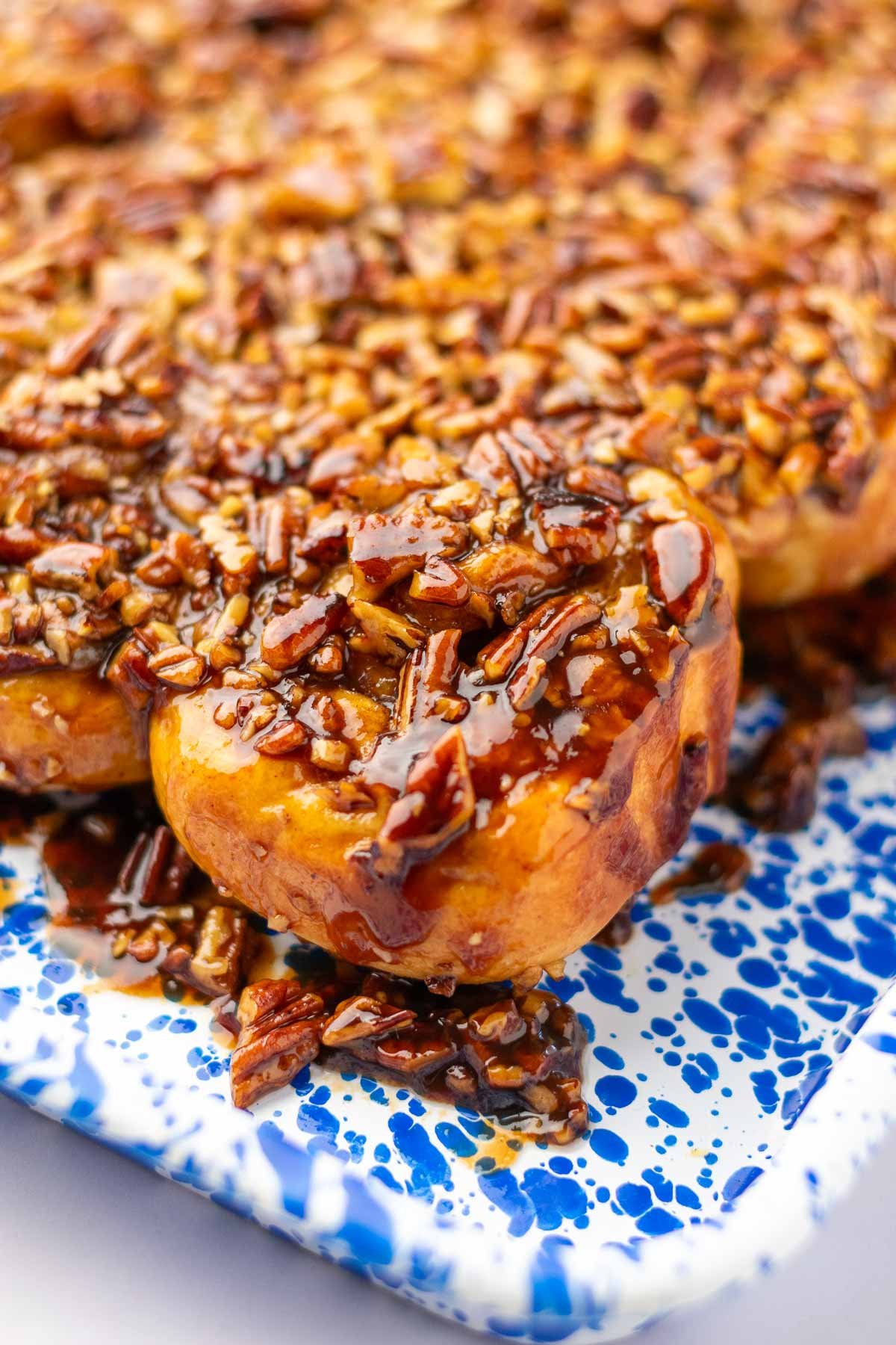Sourdough sticky buns on a platter with maple pecan topping dripping down sides.
