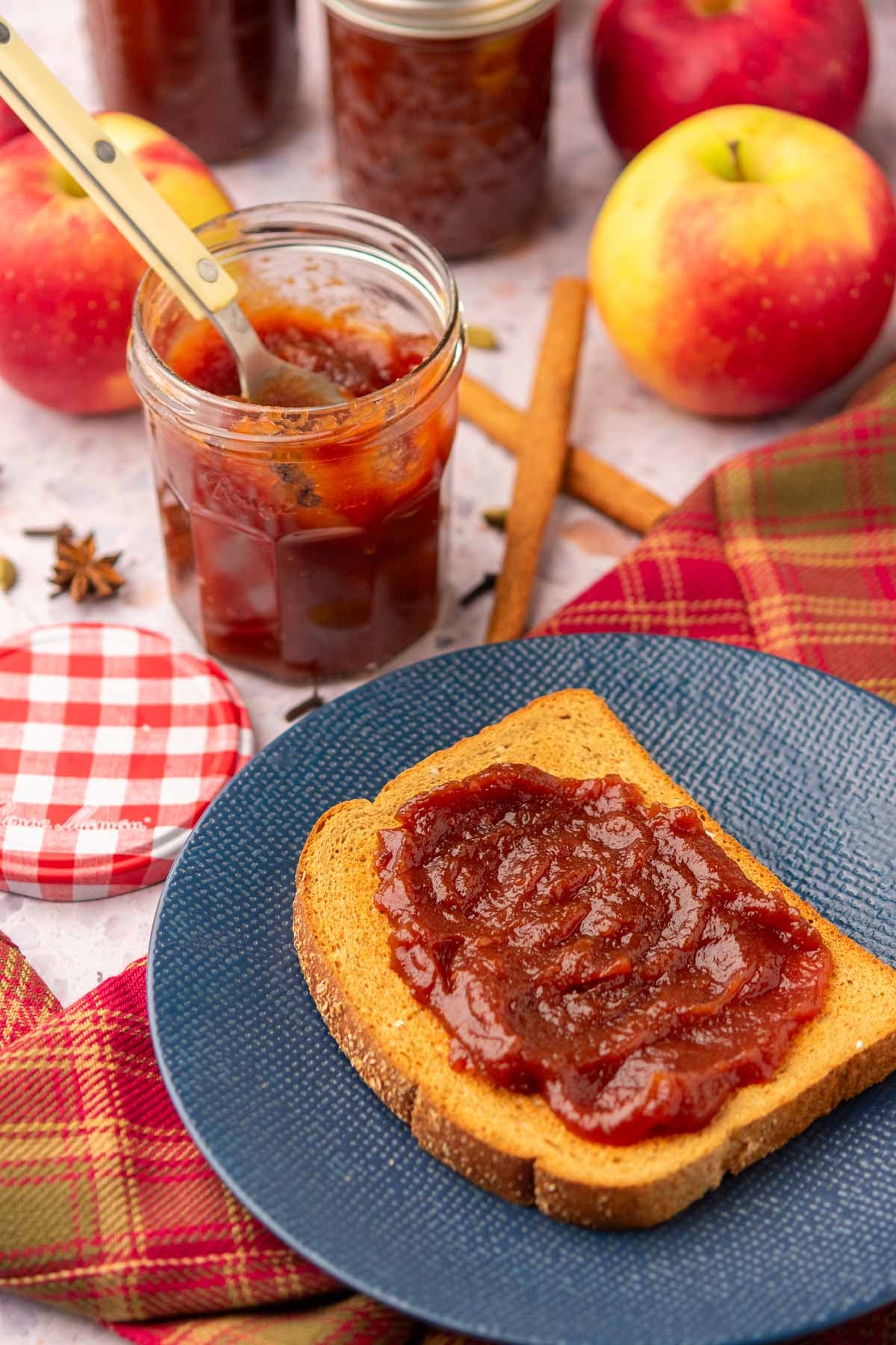 Apple butter on toast and jar of apple butter with apples and spices in the background.