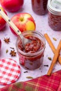 Apple butter for canning in jar with apples and spices in the background.