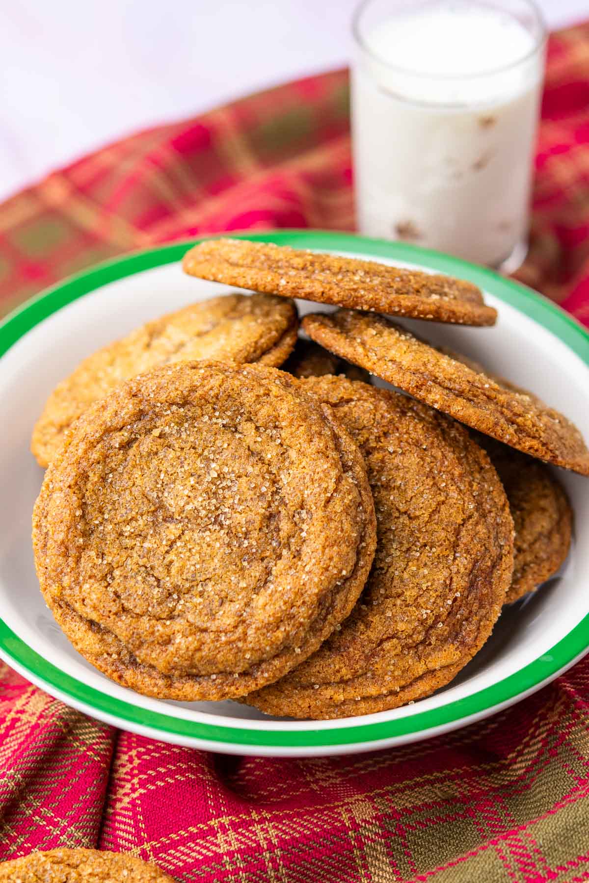 Bowl of many sourdough ginger molasses cookies on a plaid towel with a glass of milk in the background.