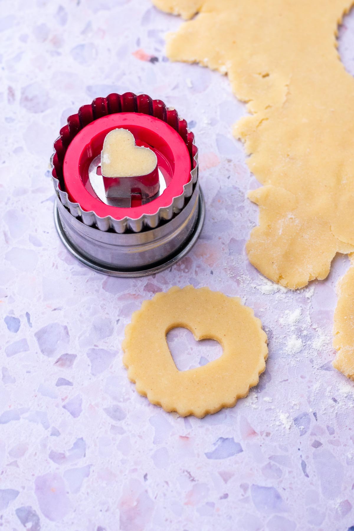 Cutting out sourdough linzer cookies with a heart cookie cutter.