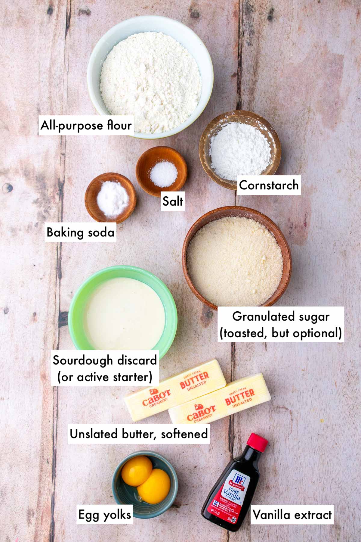 Labeled bowls of ingredients needed for sourdough sugar cookies including all-purpose flour, salt, baking soda, sugar, unsalted butter, sourdough discard, egg yolks, vanilla extract, and cornstarch.