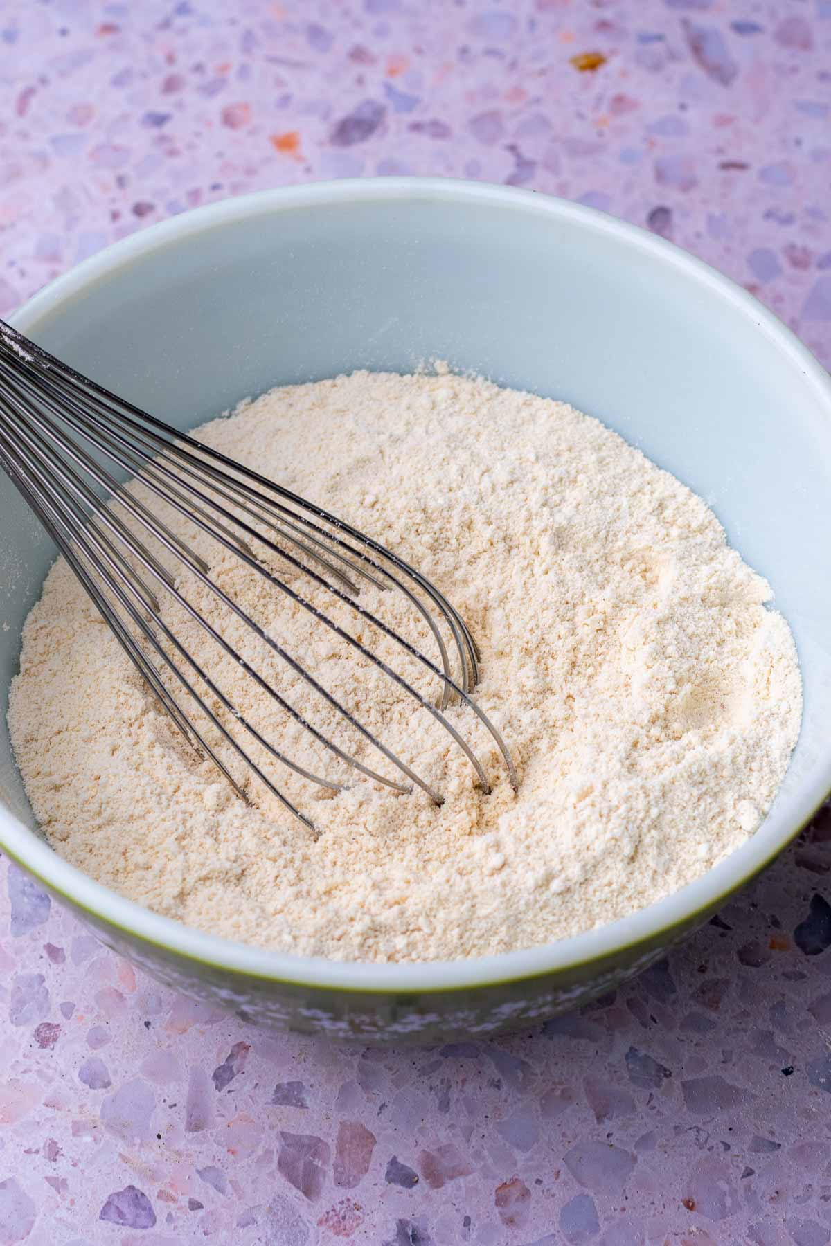 Mixing dry ingredients for sourdough linzer cookies in a bowl with a whisk.