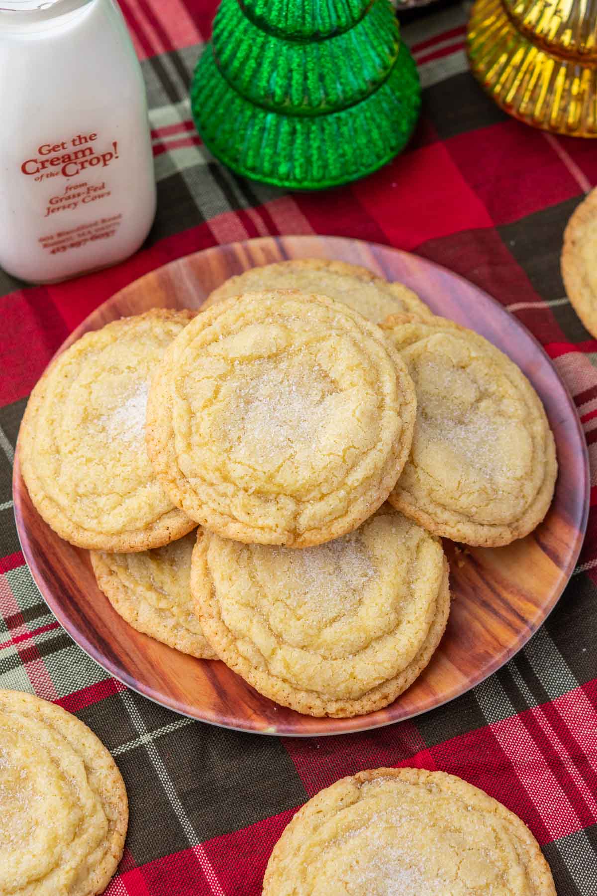 A plate of sourdough sugar cookies on a plaid towel with a glass of milk and Christmas decorations.