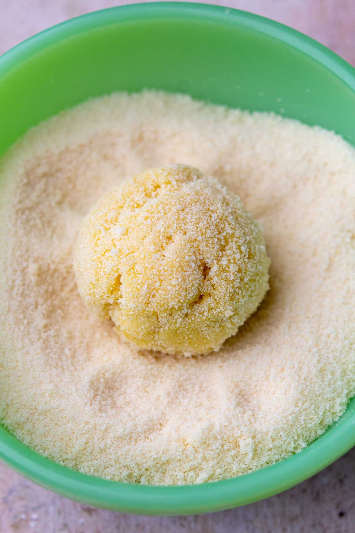 A sourdough sugar cookie ball rolled in a bowl of sugar.