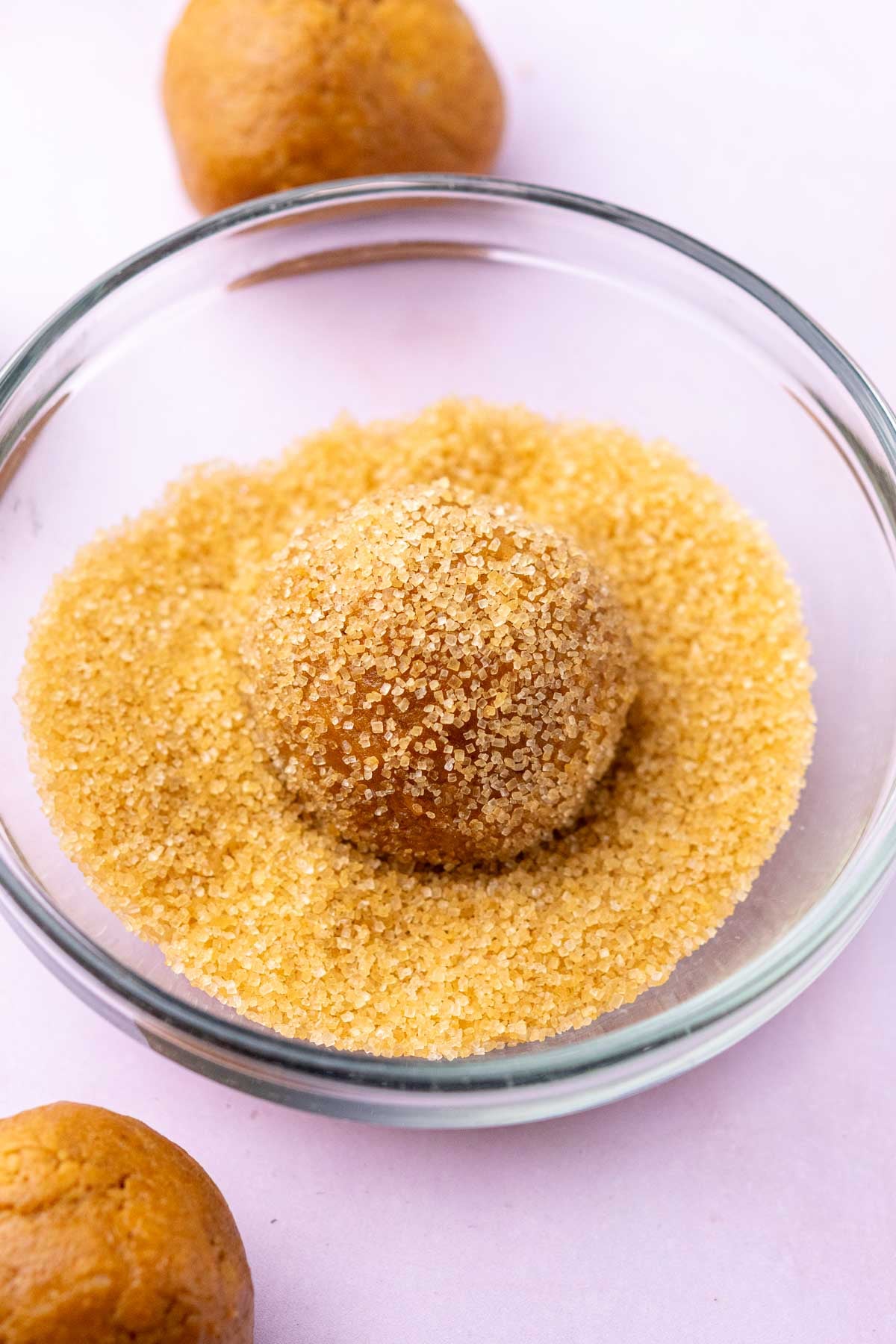 Sourdough ginger molasses cookie ball in bowl rolled in raw sugar.