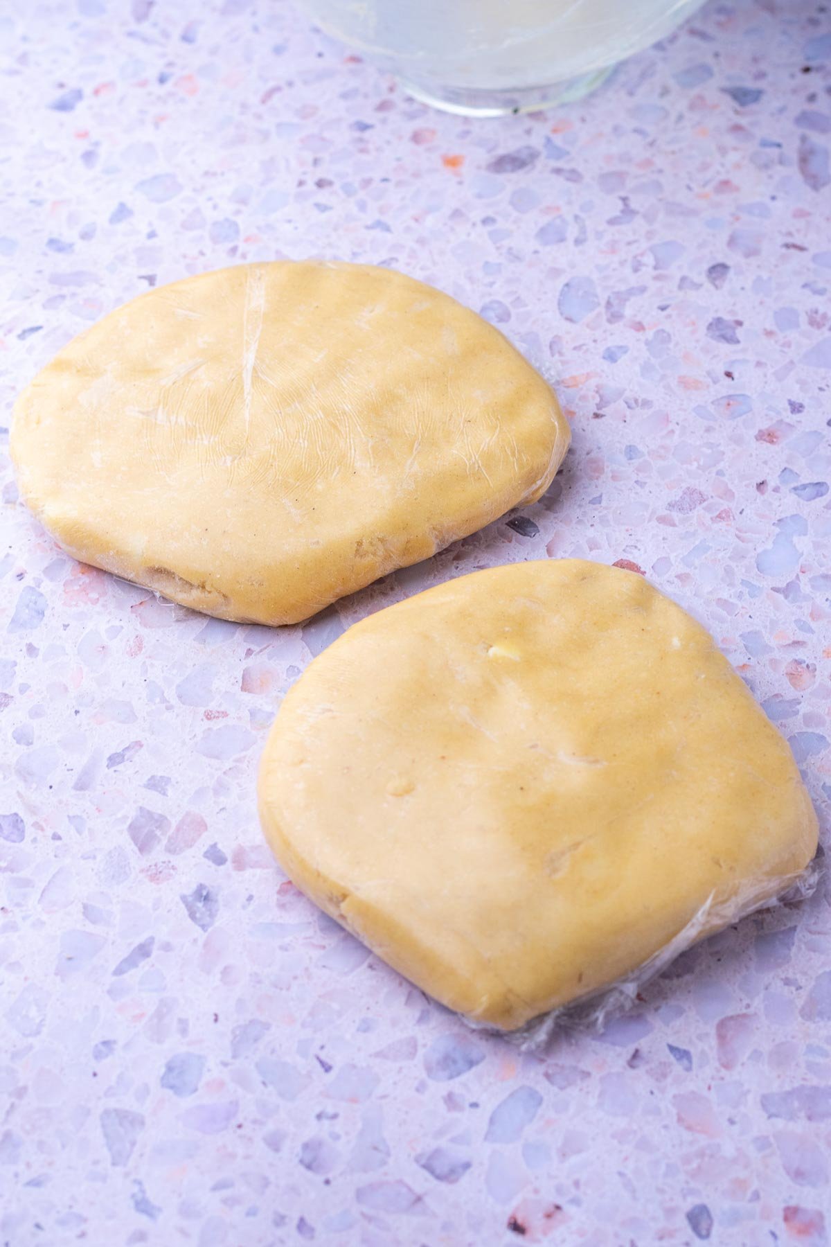 Two halves of sourdough linzer cookie dough wrapped in plastic wrap for chilling.