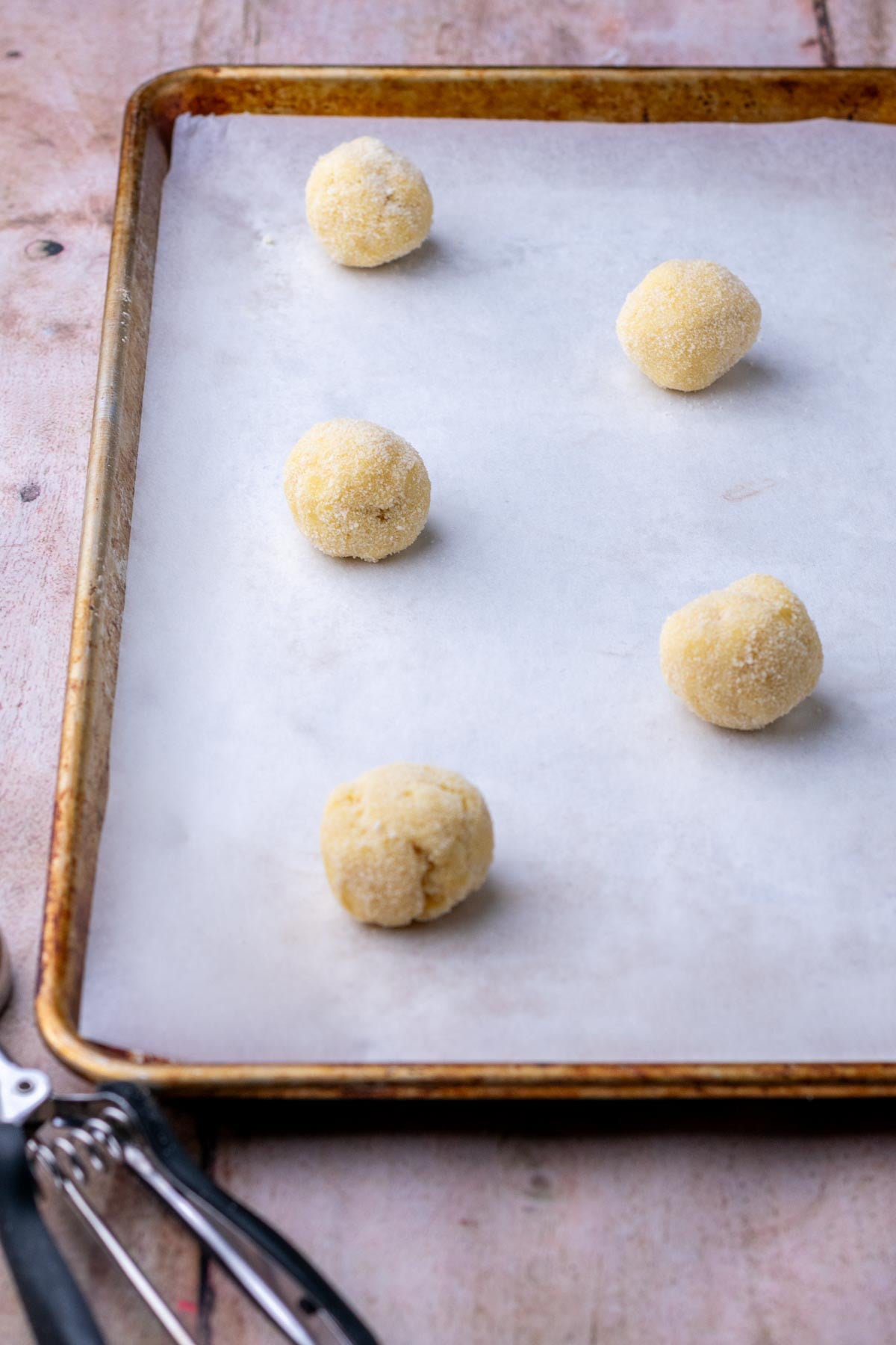 A baking sheet with unbaked sourdough sugar cookie balls and a cookie scoop.