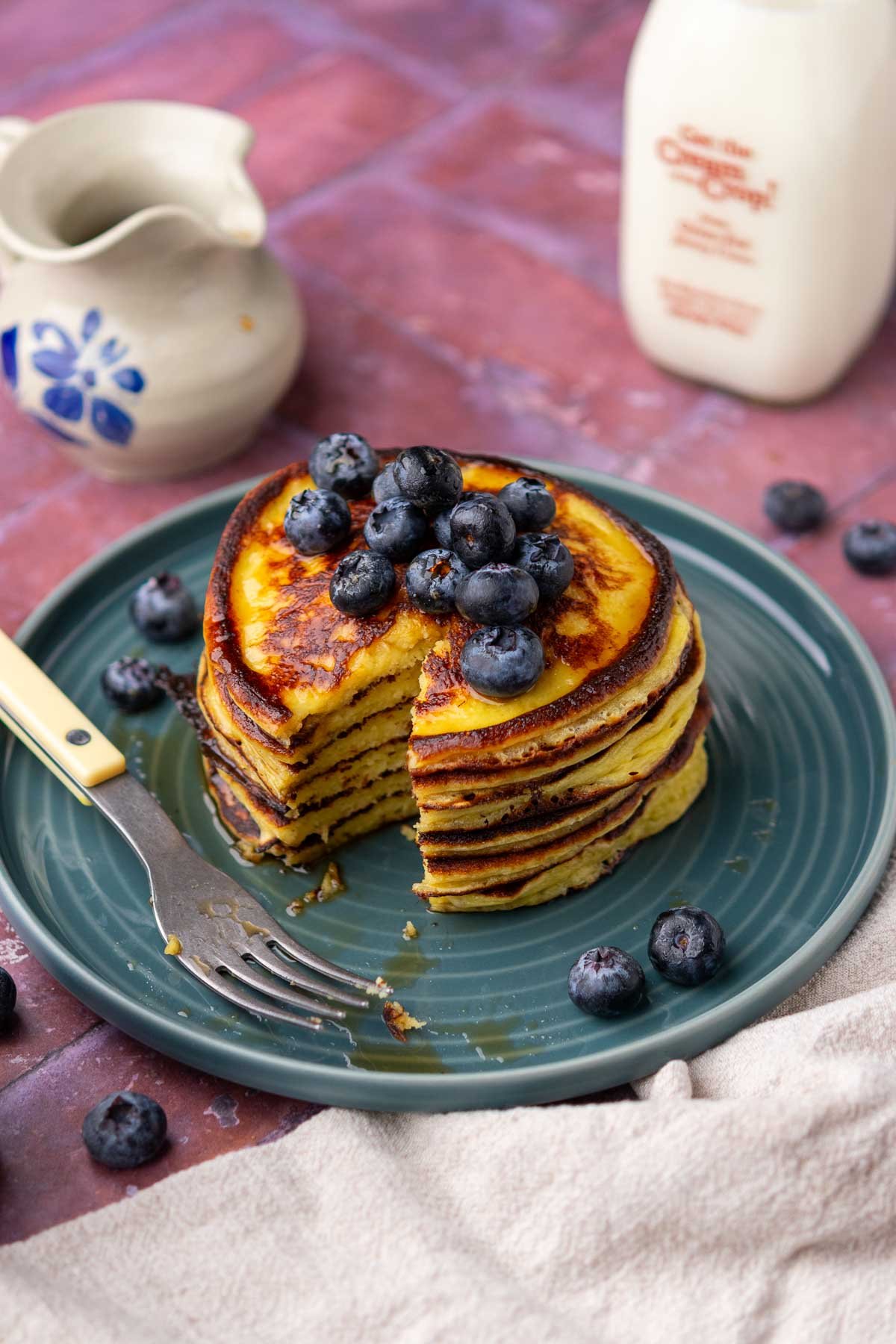 Bite taken out of a plate of sourdough cottage cheese protein pancakes with maple syrup and blueberries.