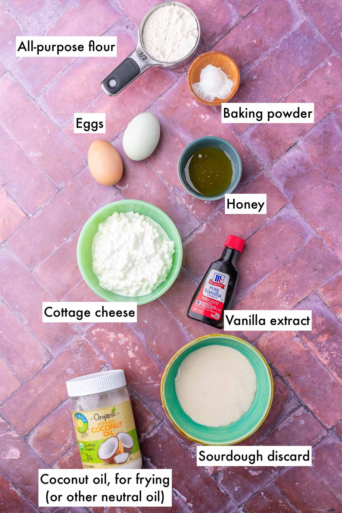 Labeled bowls of ingredients needed for sourdough cottage cheese protein pancakes including all-purpose flour, eggs, baking powder, honey, vanilla, cottage cheese, sourdough discard, and coconut oil.