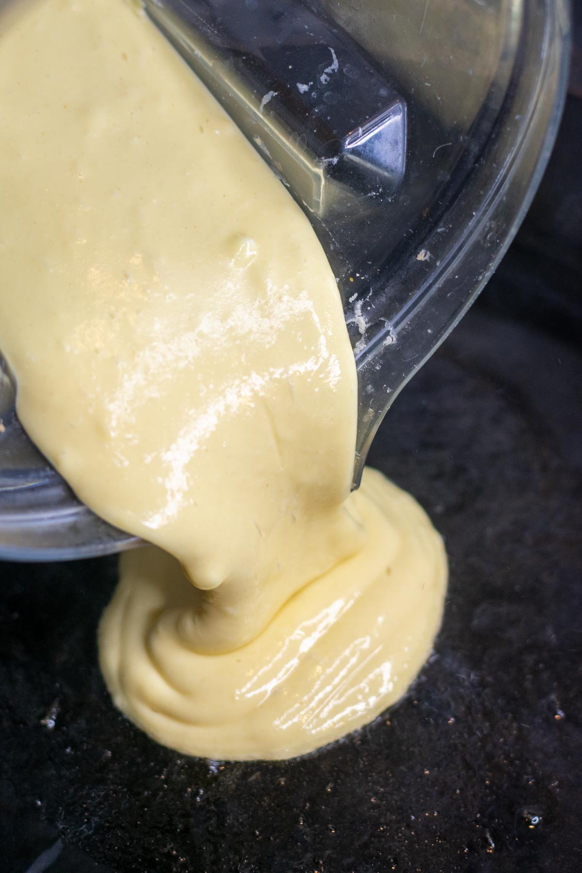Pouring sourdough cottage cheese pancake batter into cast iron skillet pan.