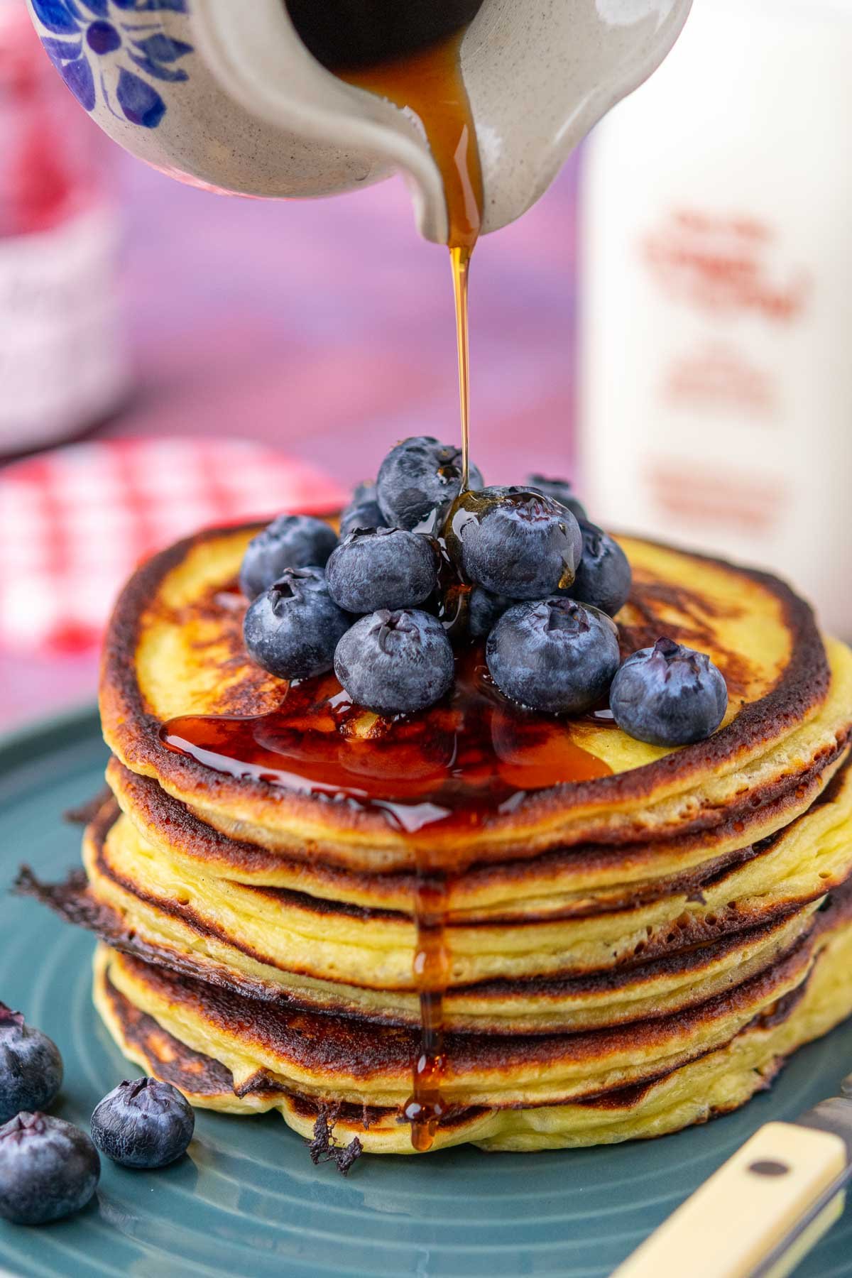 Pouring maple syrup on a stack of sourdough cottage cheese protein pancakes with blueberries.