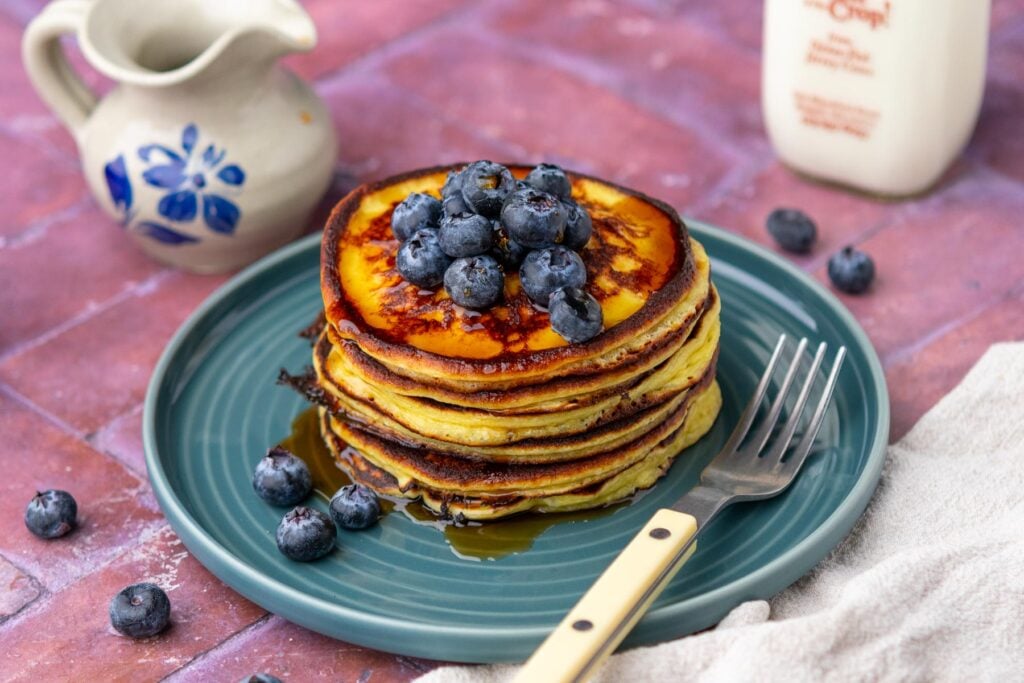 Stack of sourdough cottage cheese protein pancakes on a plate with blueberries, drizzled with maple syrup, and a fork.