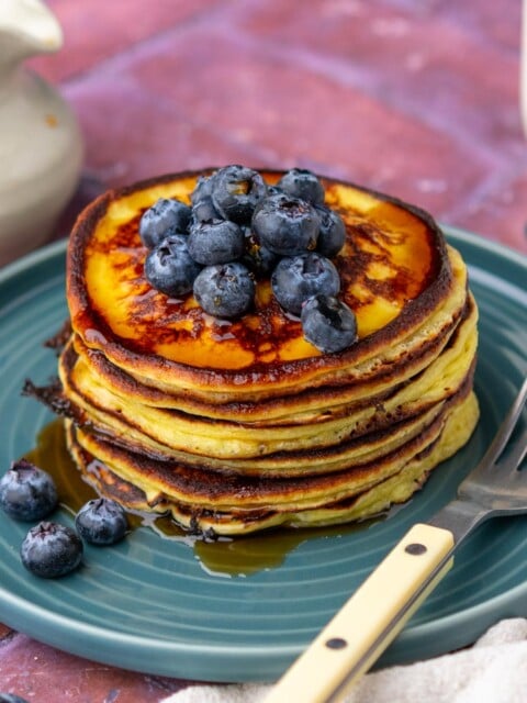 Stack of sourdough cottage cheese protein pancakes on a plate with blueberries, drizzled with maple syrup, and a fork.